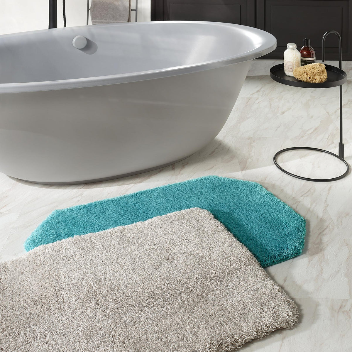 Graue Badewanne mit runden Tisch, Deko und zwei Badvorlegern auf Marmor