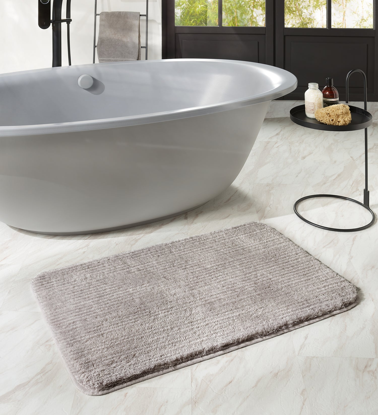 Badteppich Kleine Wolke Creativo Linea in Beige liegt vor freistehender Badewanne im modernen Badezimmer.