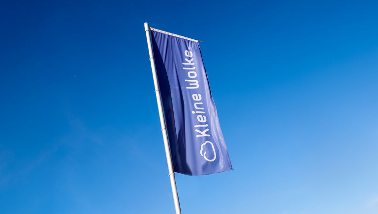 Eine blaue Kleine Wolke Fahne weht an einem Mast vor klarem Himmel.