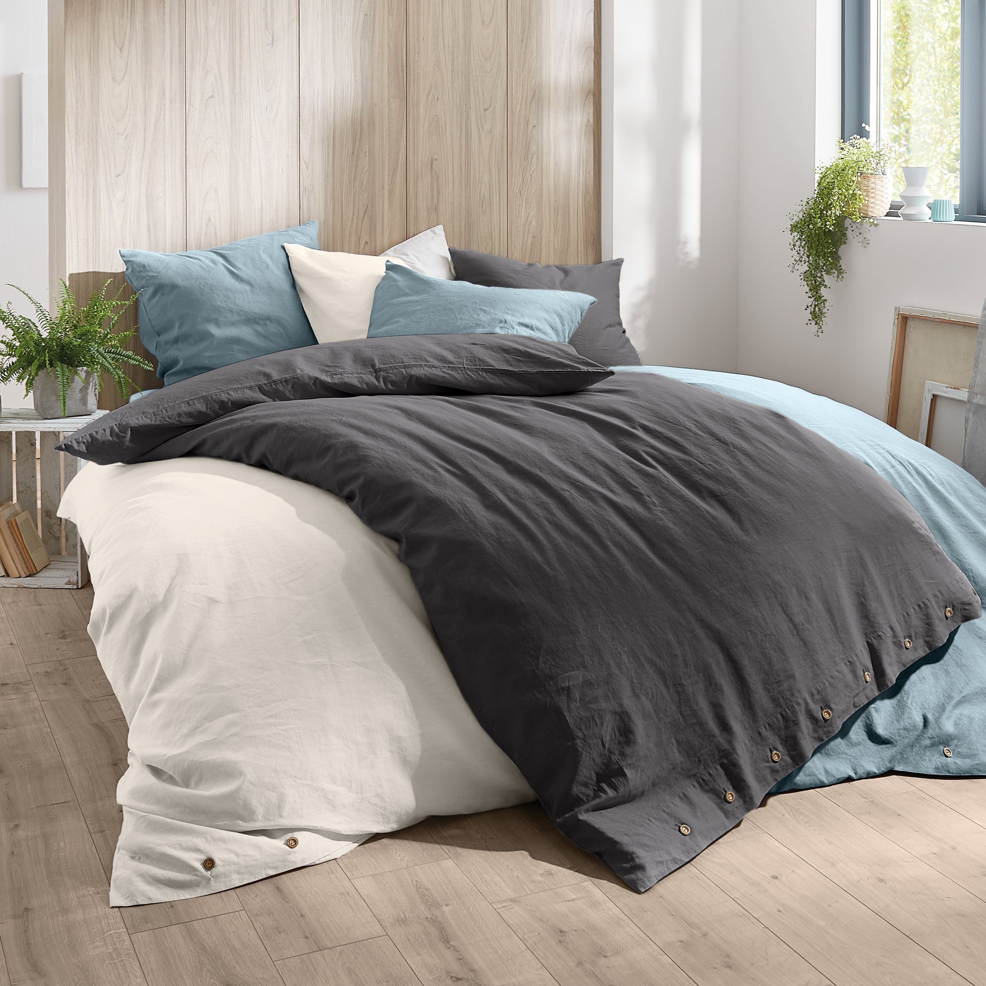 Bettwäsche Kleine Wolke zeigt zweifarbige Decken und Kissen auf einem Bett mit Holzrückwand.