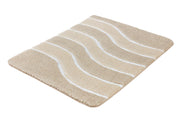 Eine beige Hochflor-Badematte mit weißen Streifen liegt auf weißem Grund.