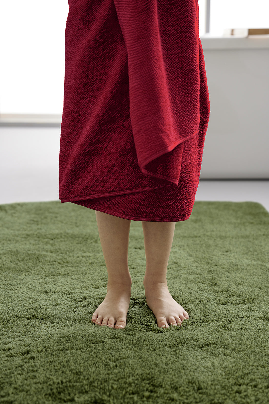 Person steht mit rotem Frottiertuch des Sets CHILL Rubin auf einem grünen Teppich.