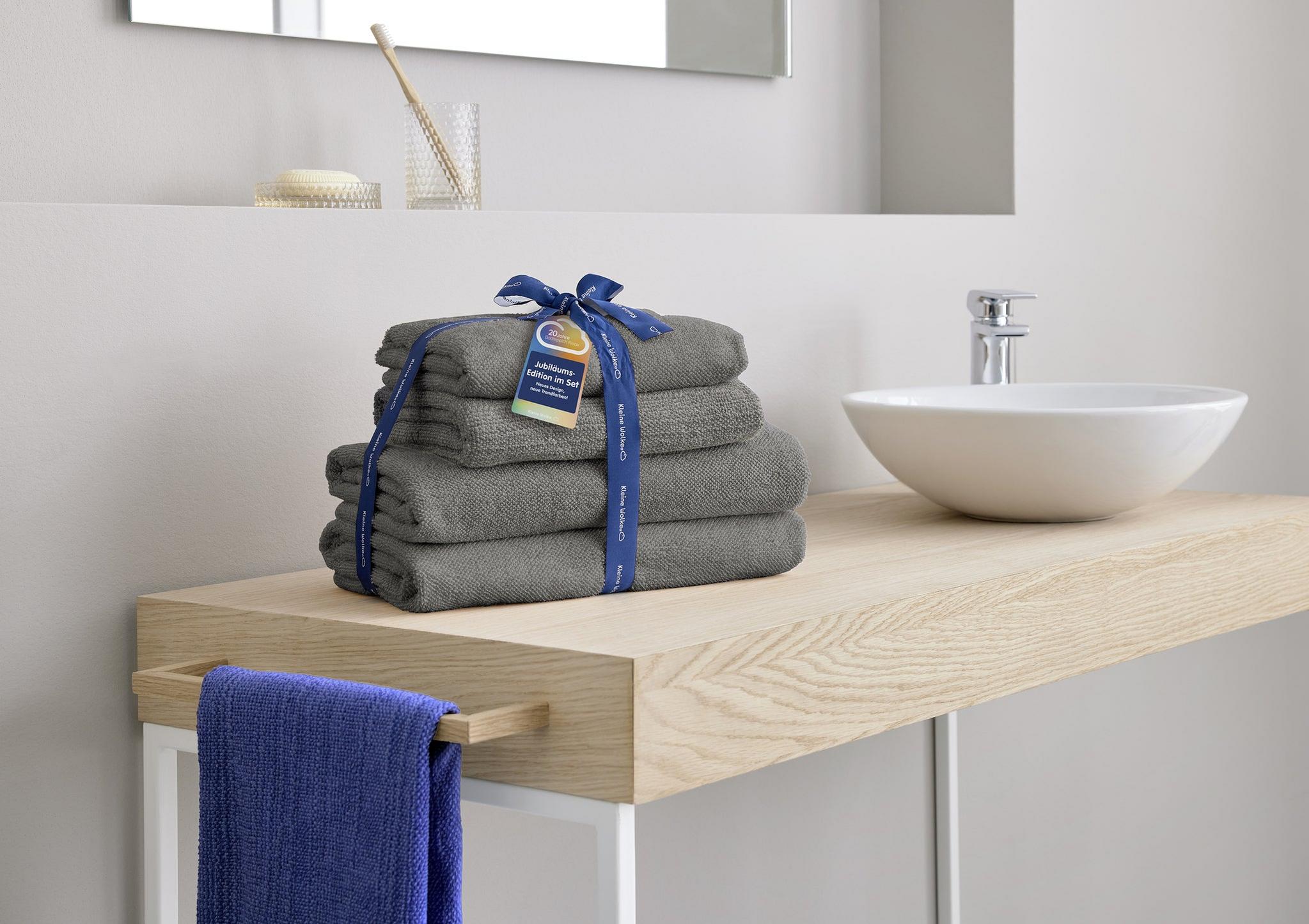 Graues Handtuch-Set mit Schleife auf Holzwaschtisch neben Waschbecken
