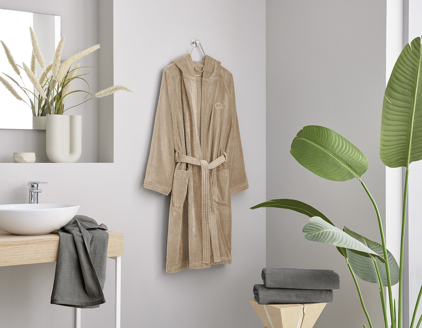 Beiger Bademantel hängt im modernen Bad neben Waschbecken und Handtüchern