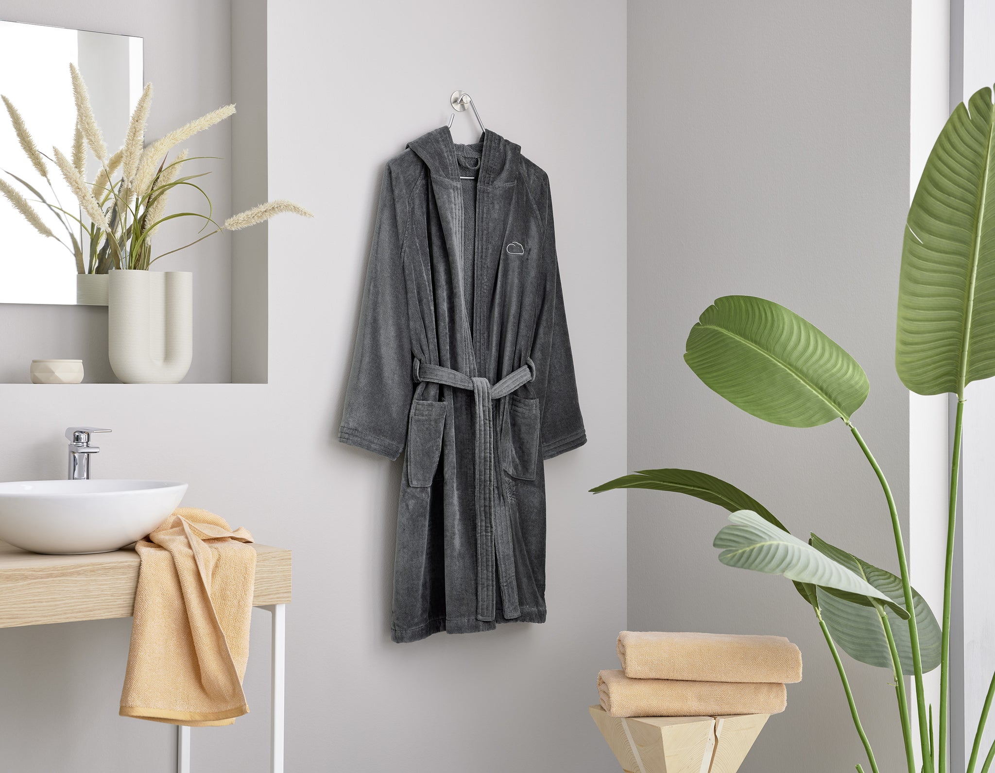Grauer Bademantel mit Kapuze hängt im modernen, hellen Badezimmer