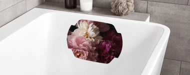 Weiße Badewanne mit Blumenkissen, Kerze und Badeschwamm am Rand aus Stoff