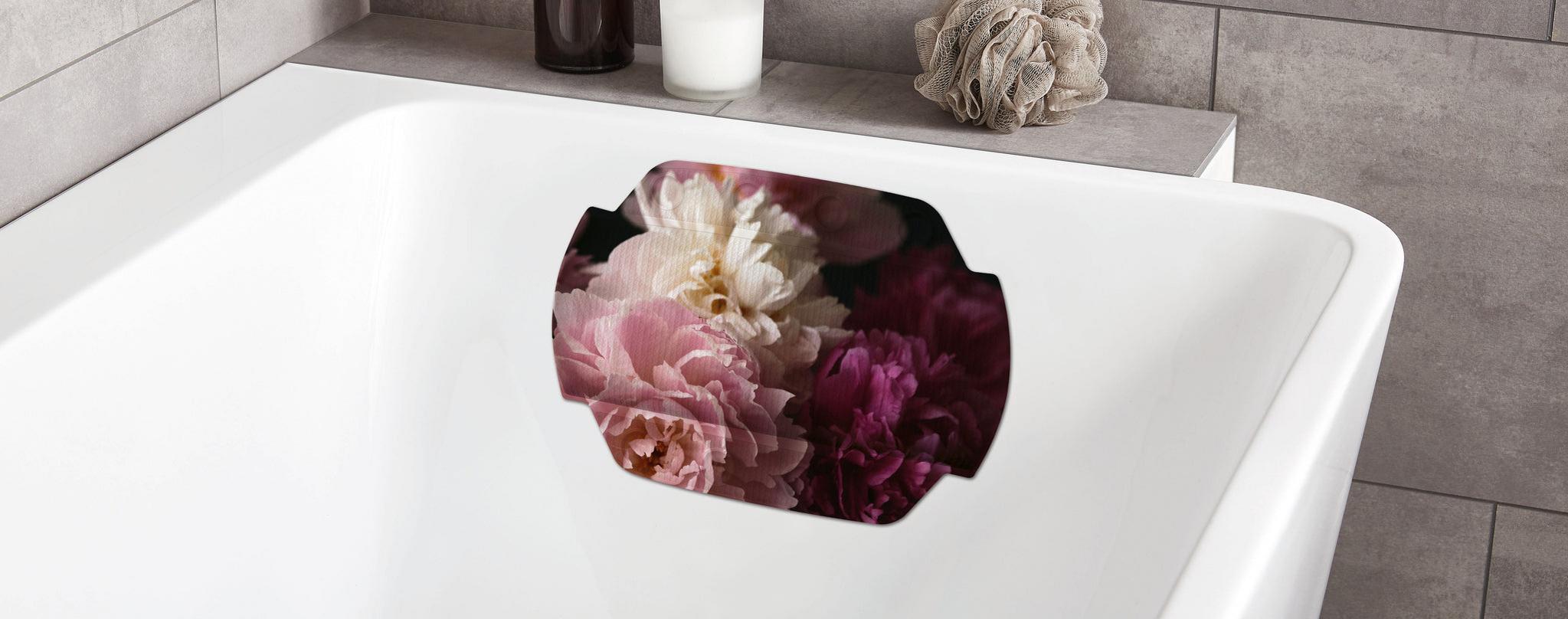 Weiße Badewanne mit Blumenkissen, Kerze und Badeschwamm am Rand aus Stoff