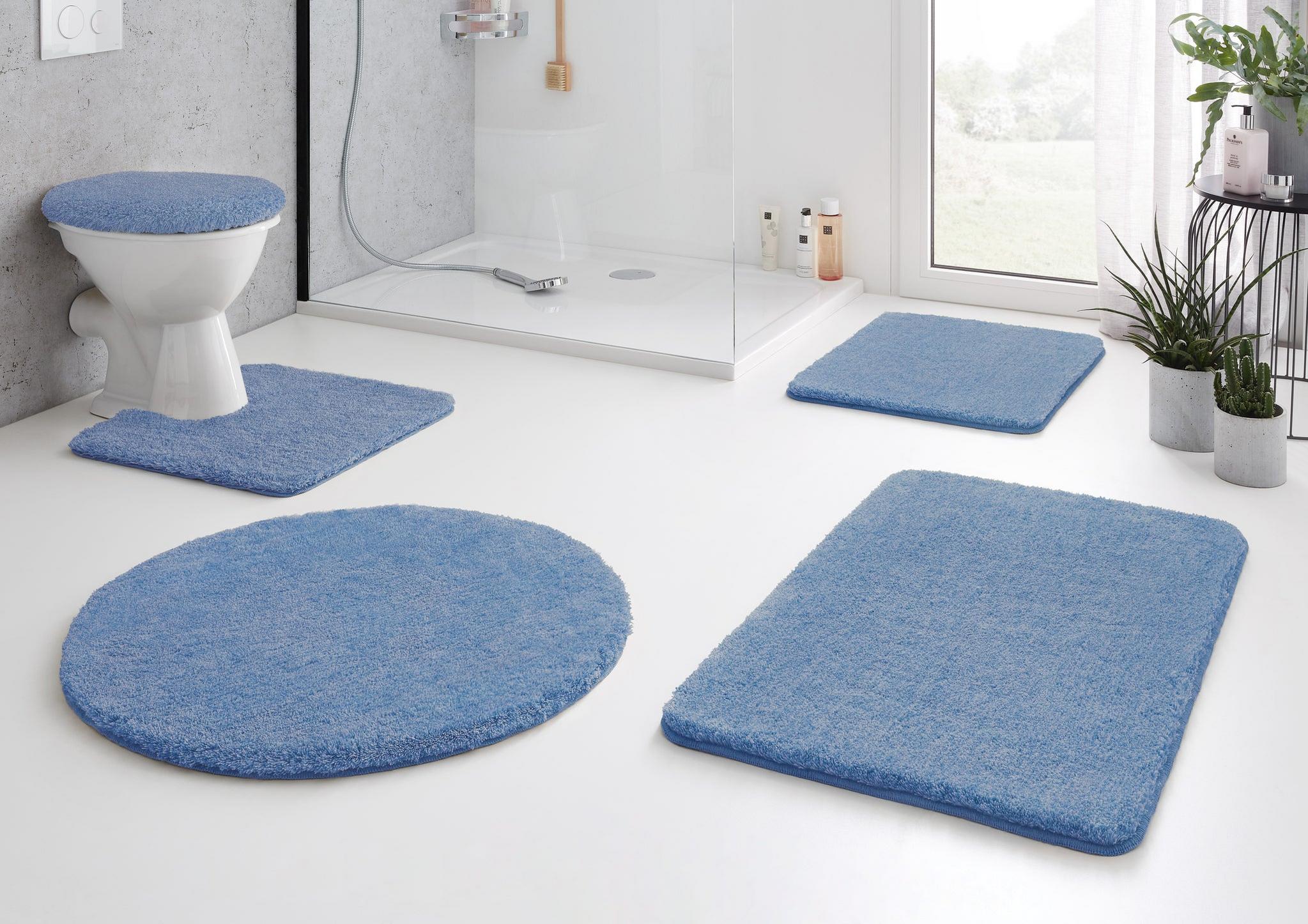 Modernes Bad mit blauen Badematten-Set und WC-Deckelbezug auf weißem Boden