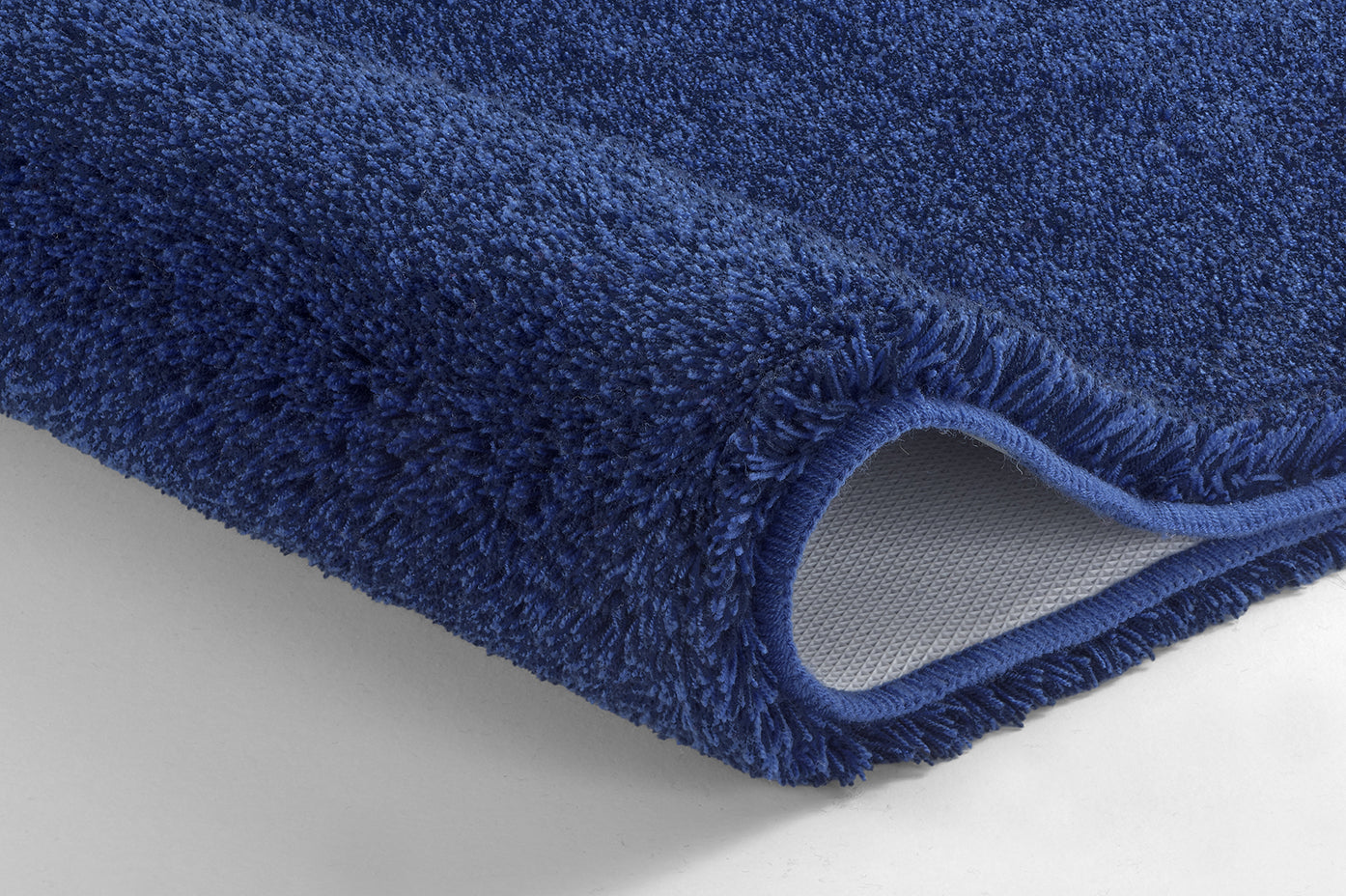 Nahaufnahme einer blauen Badematte mit umgeschlagener Ecke und Rückseite