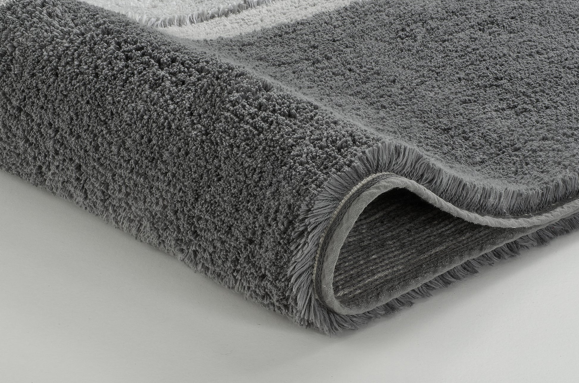 Graue, dichtflorige Badematte in Nahaufnahme auf hellem Untergrund