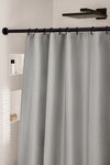 Grauer Duschvorhang an schwarzer Stange vor weißer Duschwand mit Ablagen