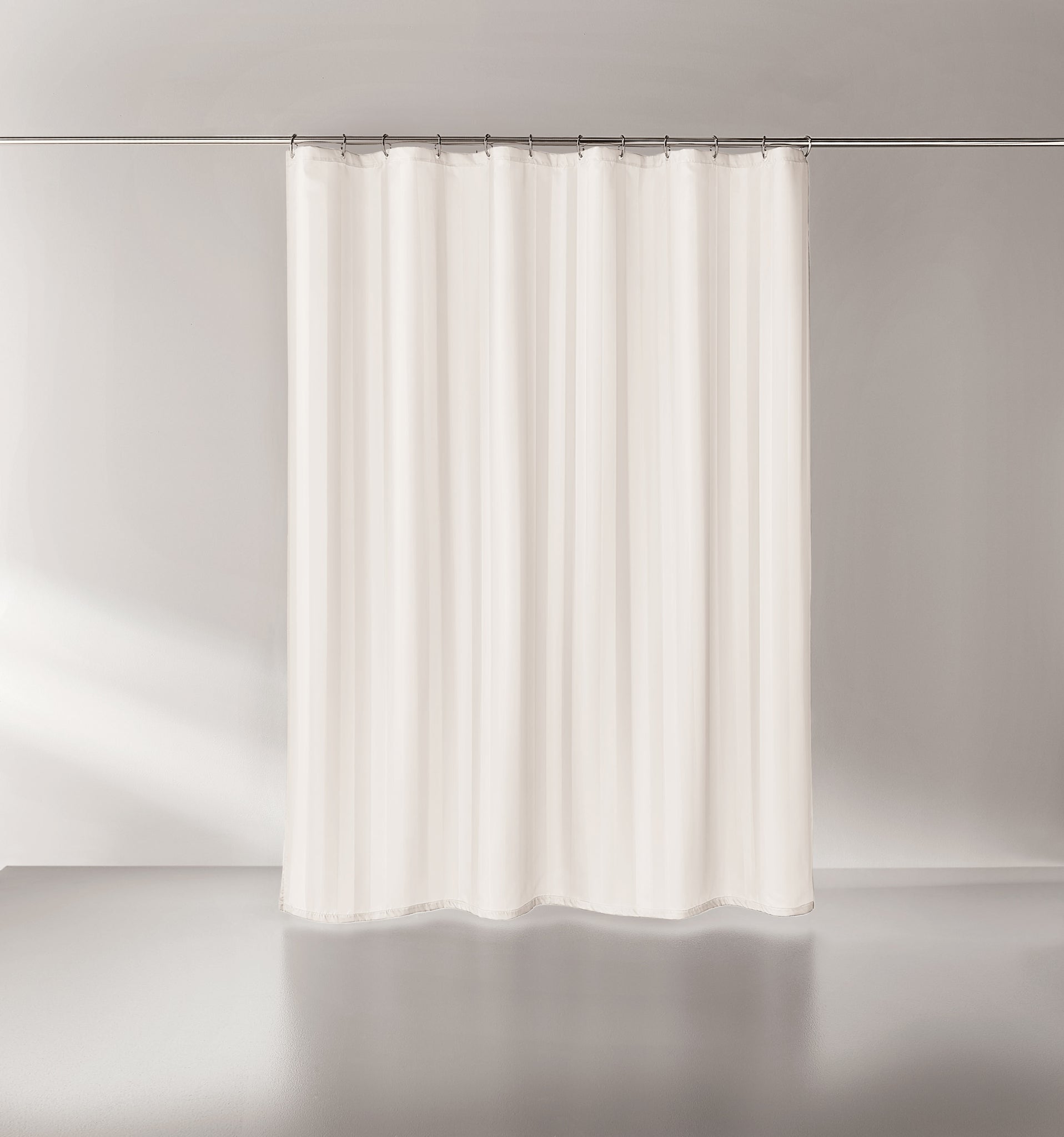 Weißer, schlichter Duschvorhang an Metallstange vor hellgrauer Wand