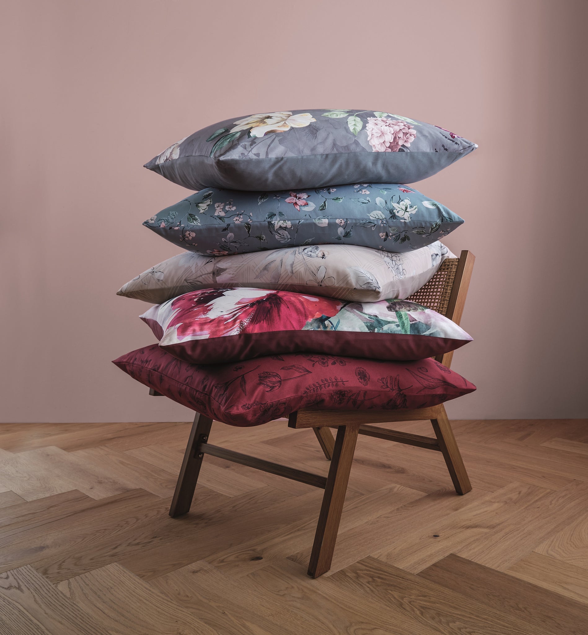 Rotes Satin-Bettwäsche-Set LISSE mit floralem Kissen auf Holzstuhl vor rosa Wand.