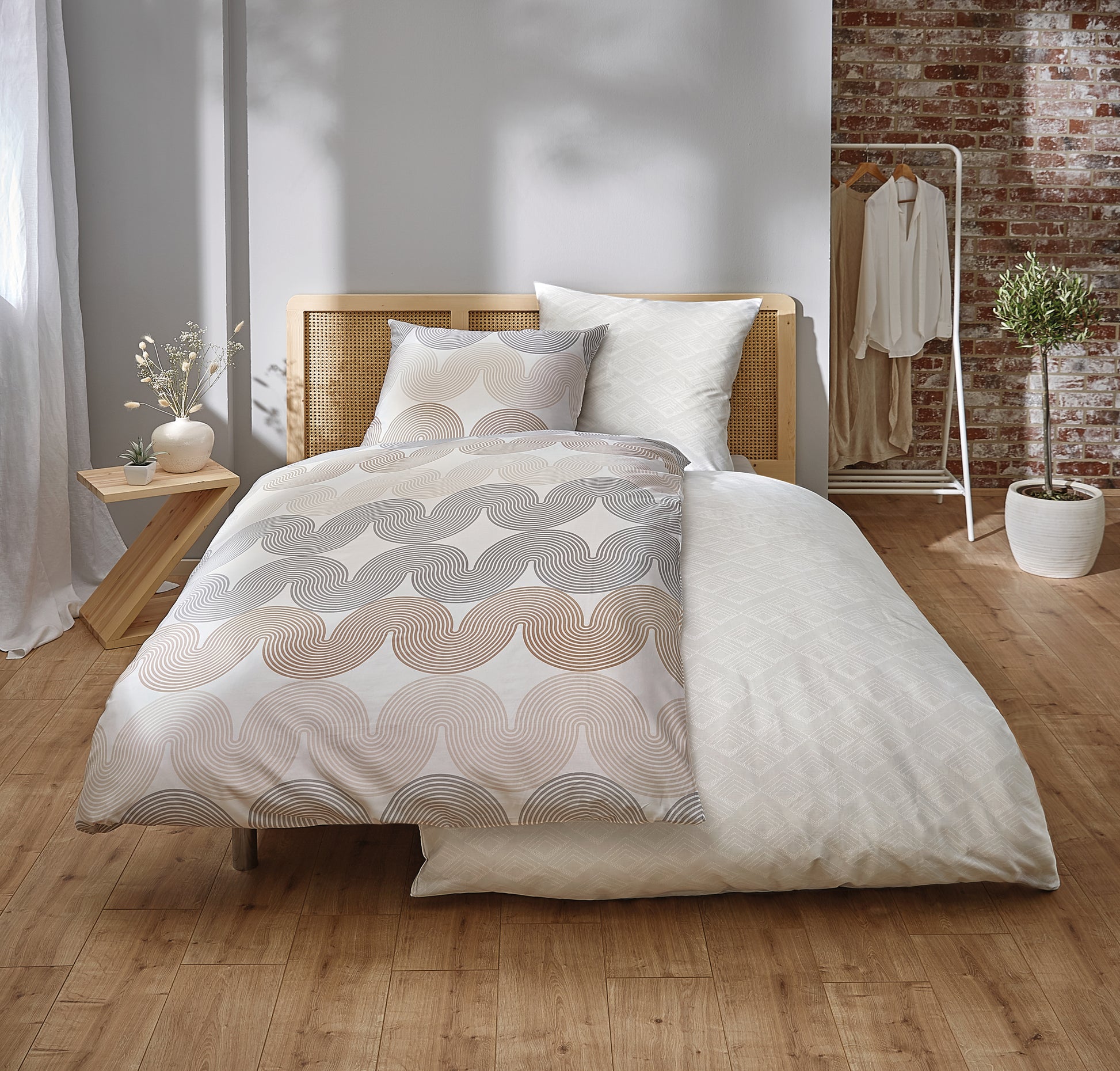 Modernes Bett mit beigefarbener Bettwäsche vor Backsteinwand in hellem Raum