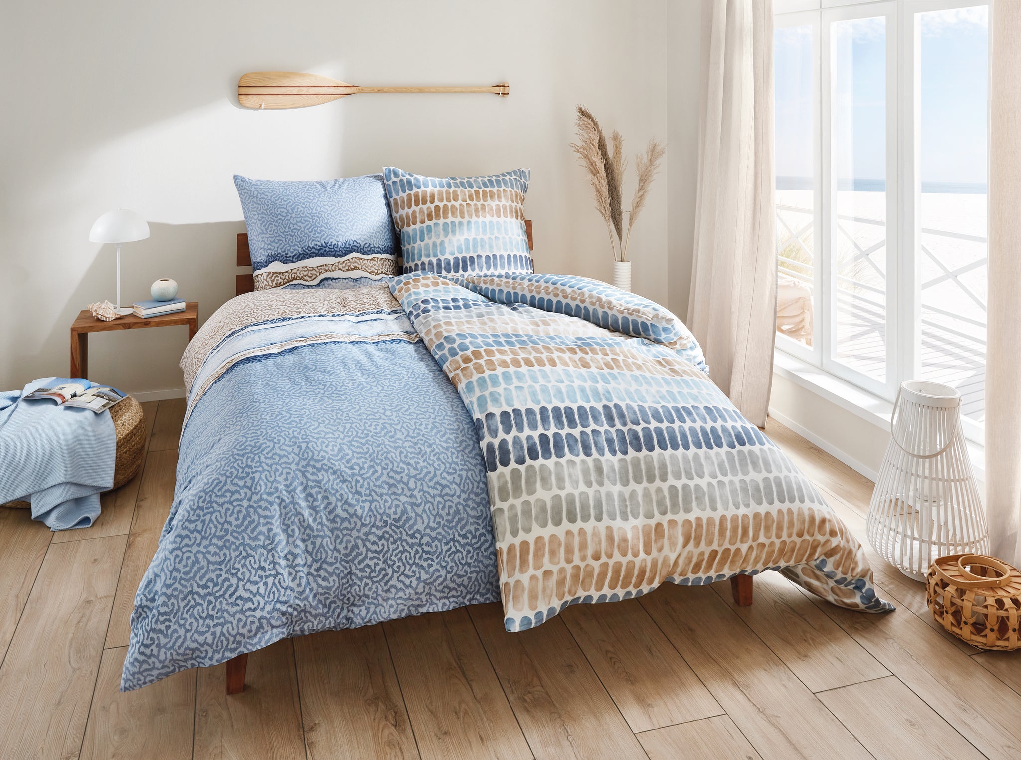 Helles Schlafzimmer mit Bett in blau-gemusterter Bettwäsche am Fenster