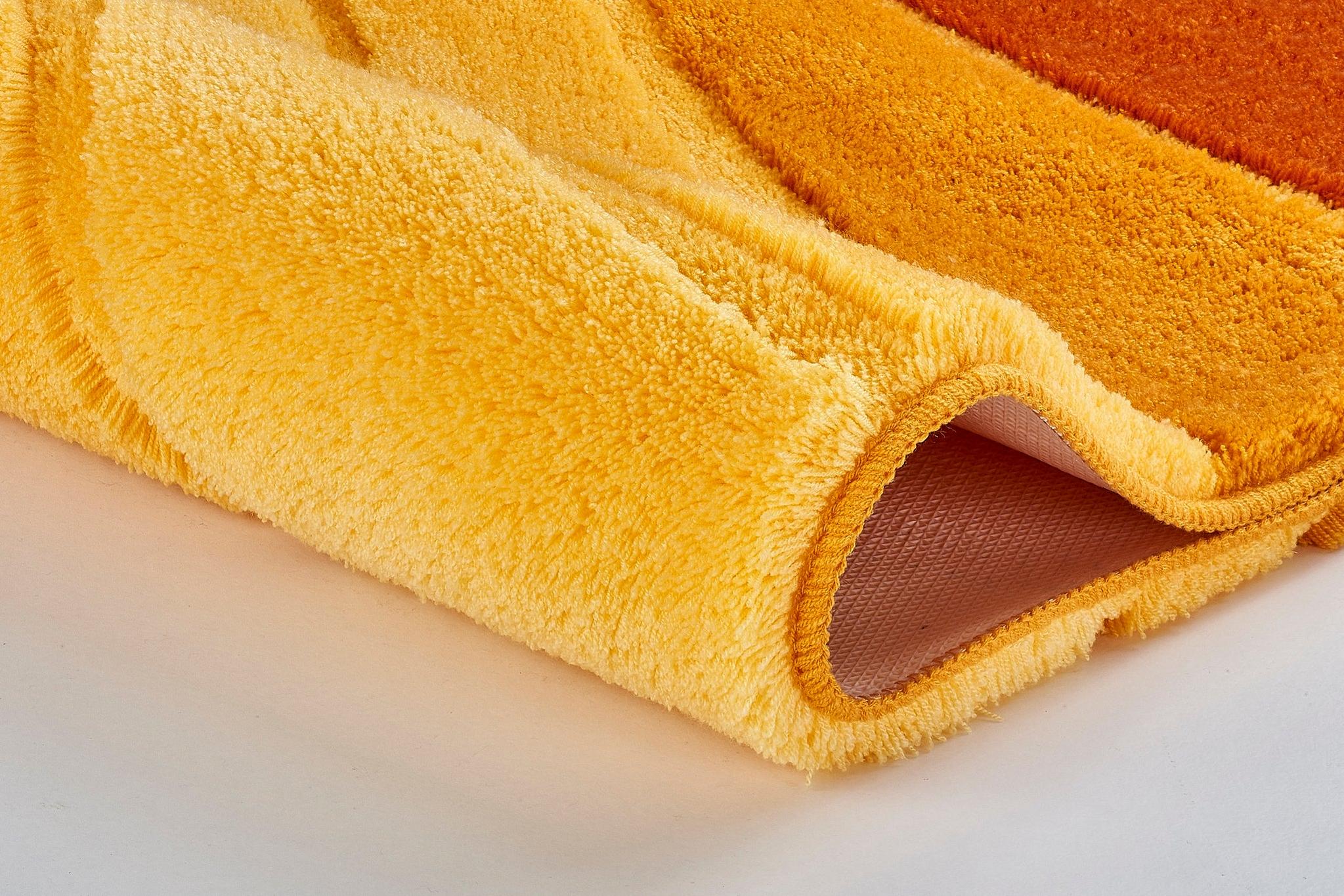 Nahaufnahme eines gelb-orangen, flauschigen Badteppichs gerollt leicht