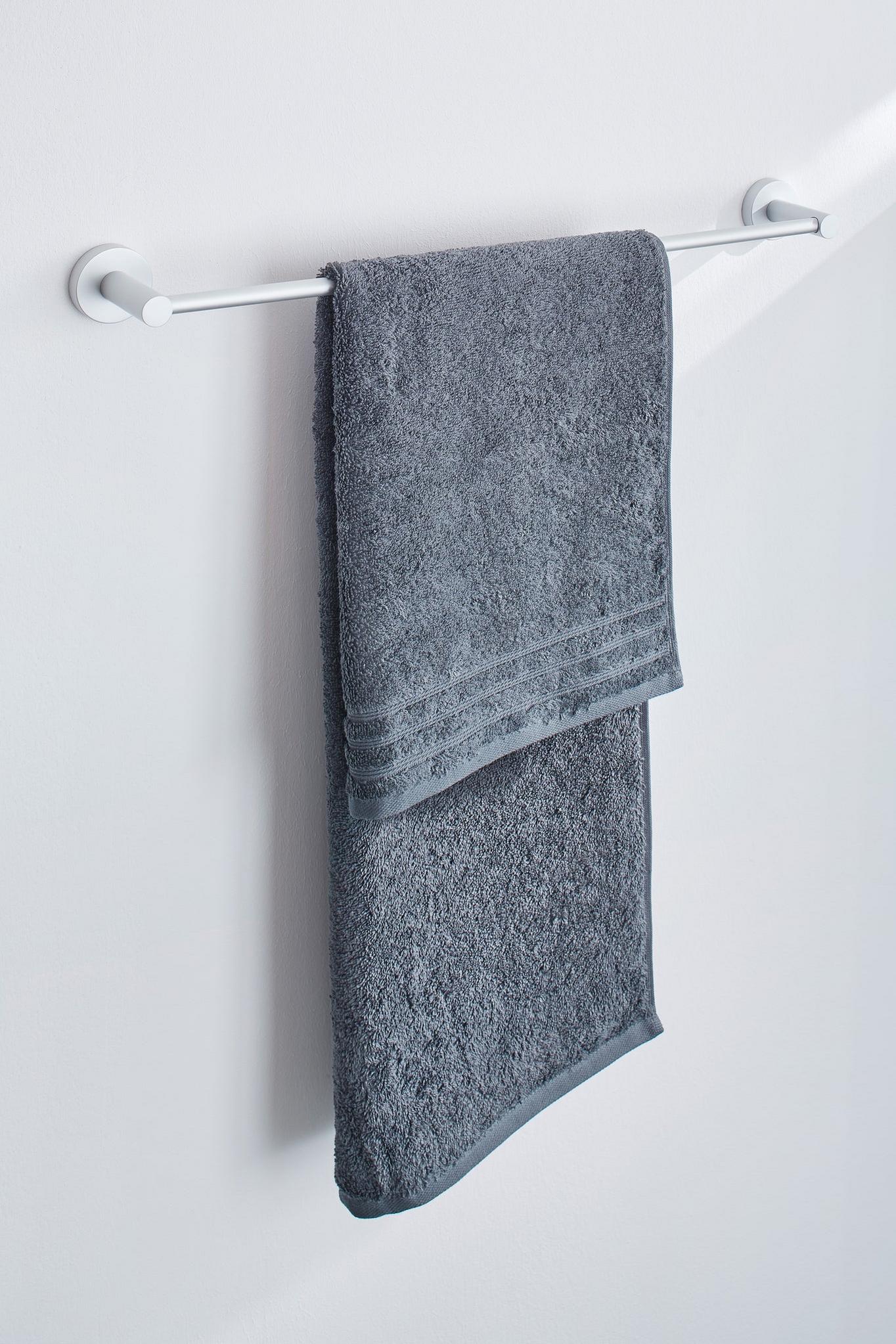 Graues Handtuch auf weißer Handtuchstange vor heller Badezimmerwand