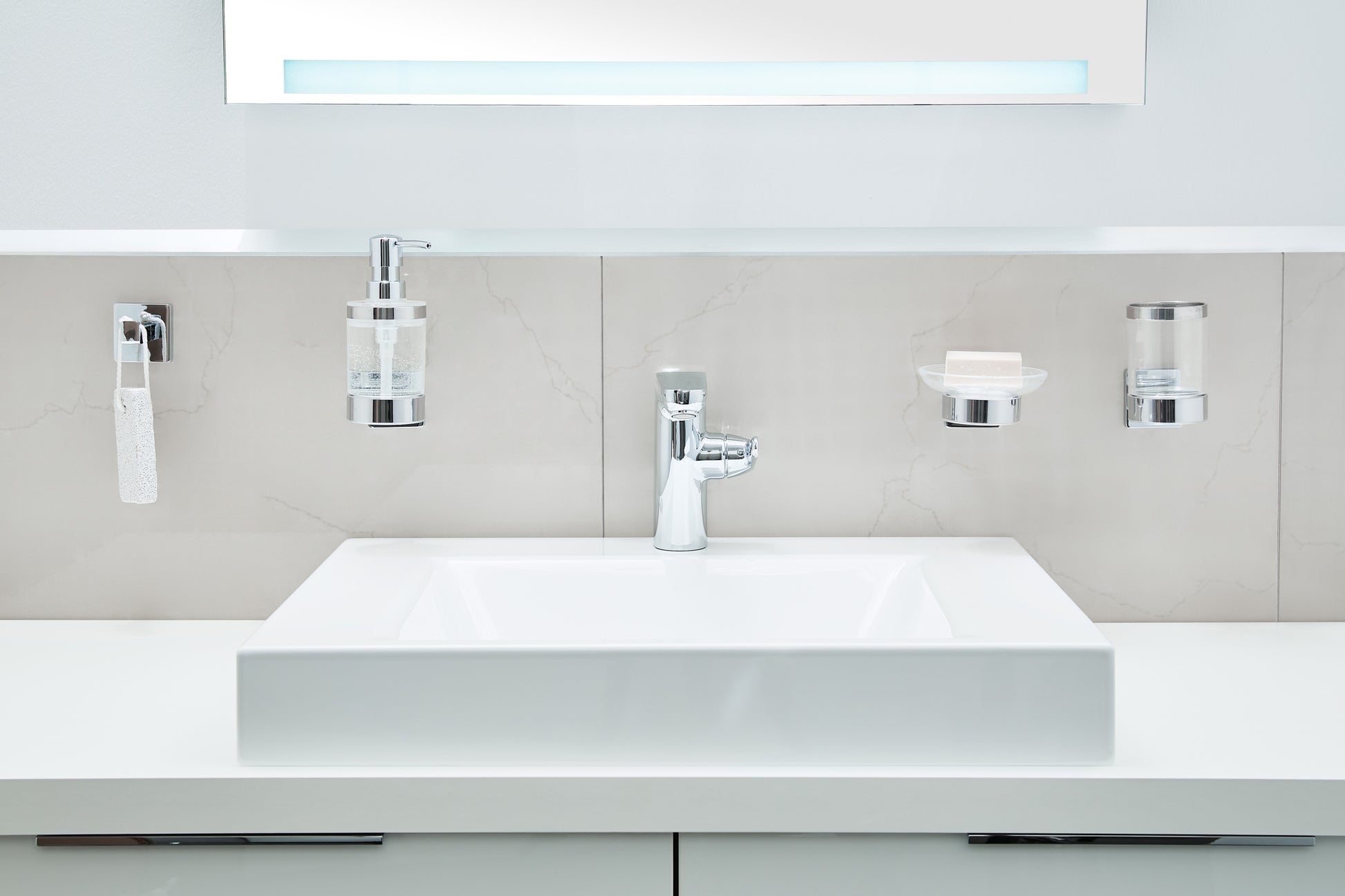 Wand-Seifenspender LUNO Clear aus Glas neben passendem Badzubehör über weißem Waschbecken.