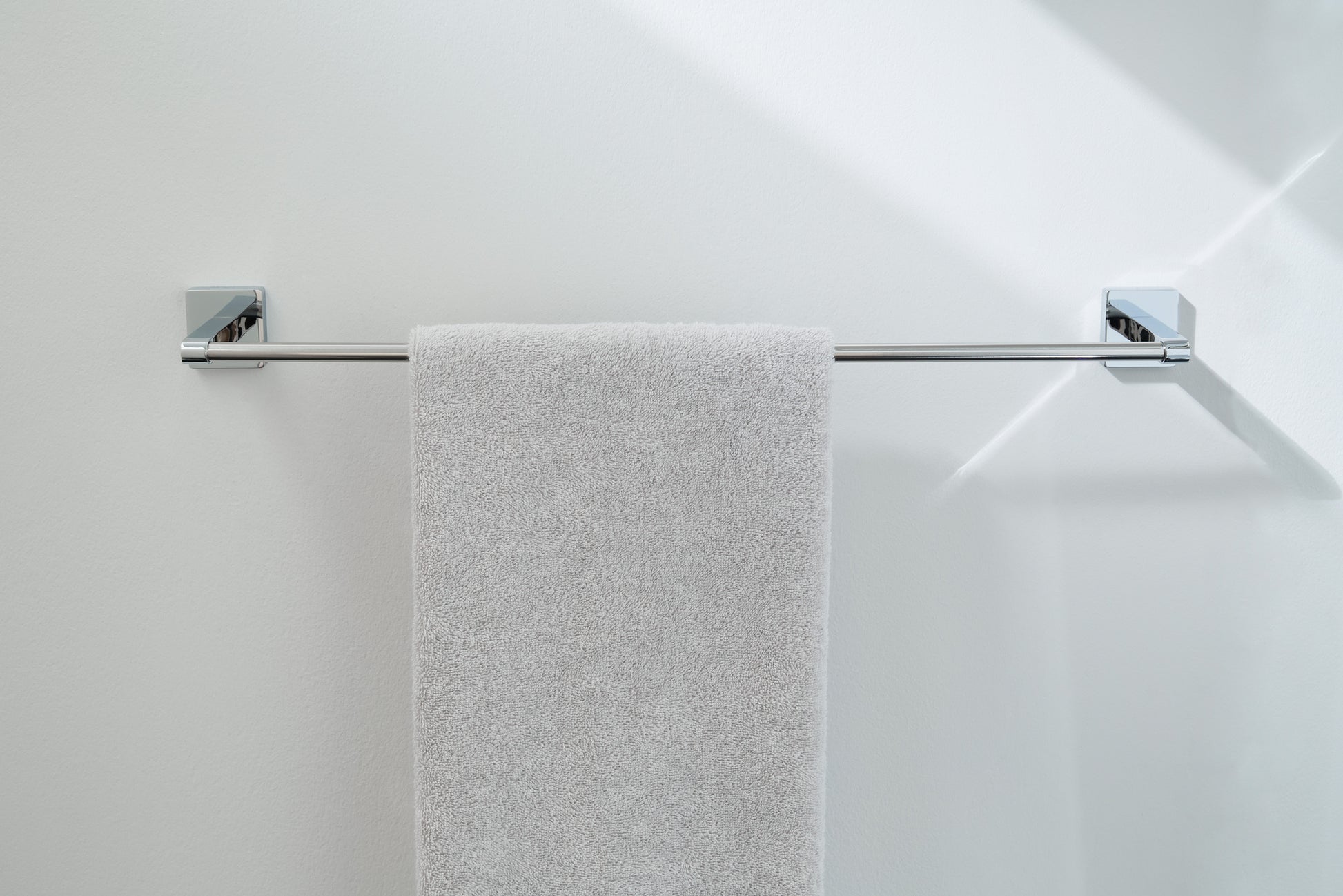 Das Bild zeigt die Handtuchstange LUNO silberfarben an weißer Wand mit hellem Handtuch.
