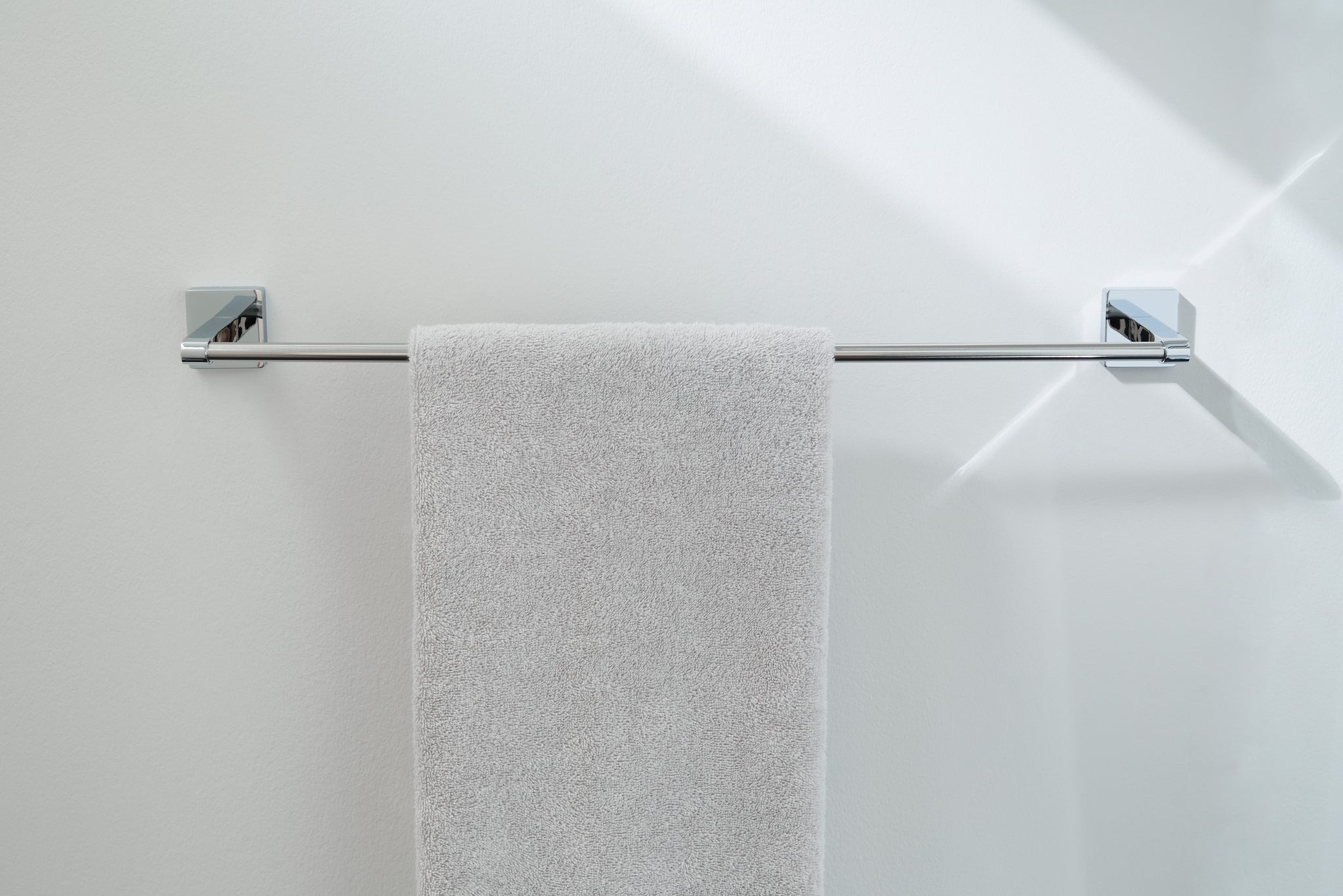 Das Bild zeigt die Handtuchstange LUNO silberfarben an weißer Wand mit hellem Handtuch.