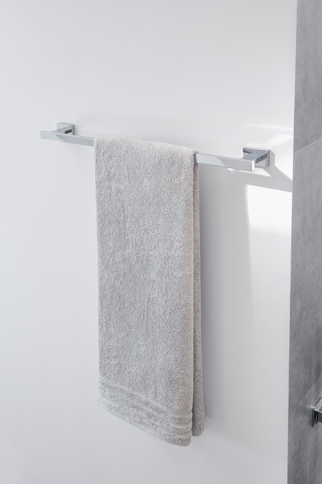 Chrom-Handtuchhalter mit grauem Handtuch an weißer Badezimmerwand