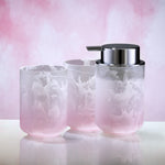 Zwei rosa-weiße Becher und Seifenspender aus Glas vor rosa Hintergrund