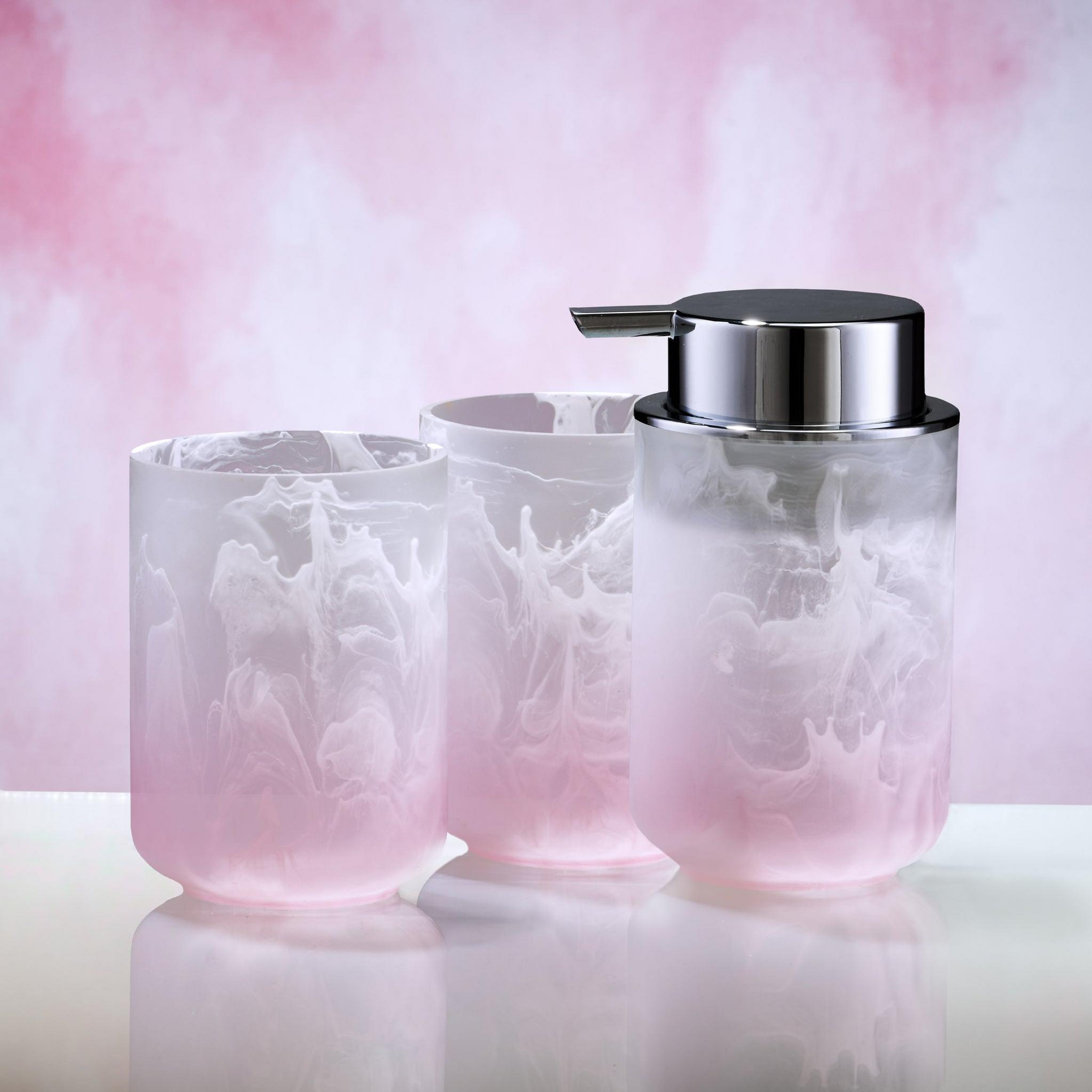 Zwei rosa-weiße Becher und Seifenspender aus Glas vor rosa Hintergrund