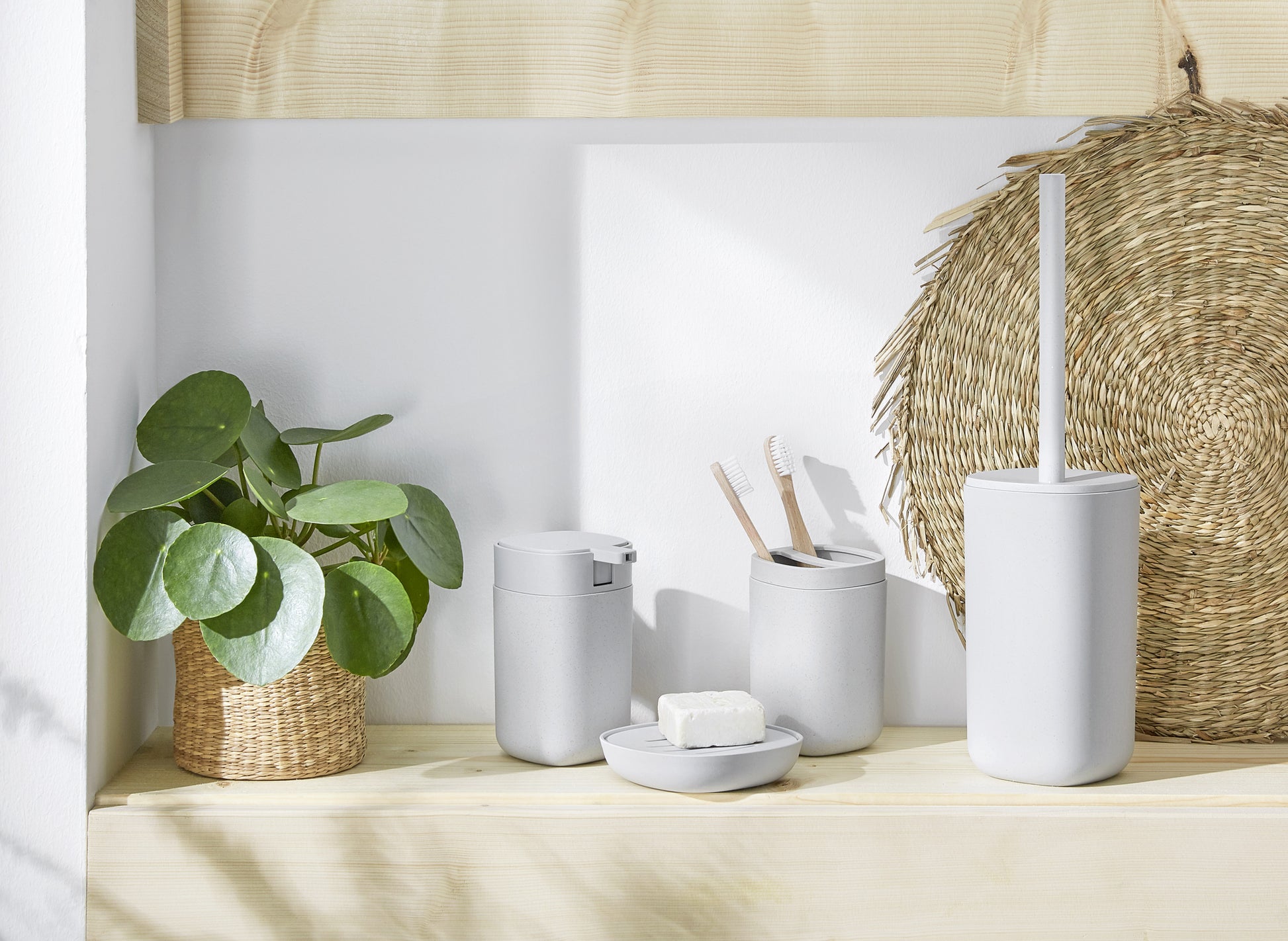 Helles Bad-Set aus hellgrauen Accessoires mit Pflanze im Korb auf Holzablage