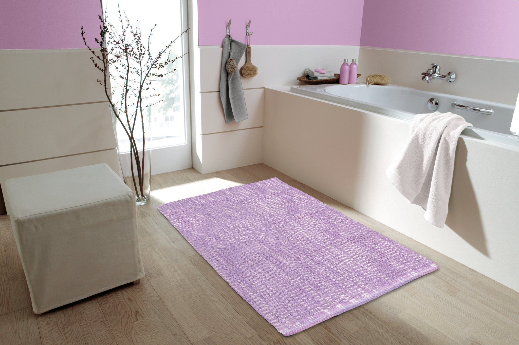 Helles Bad mit rosa rechteckigem Badvorleger vor weißer Badewanne