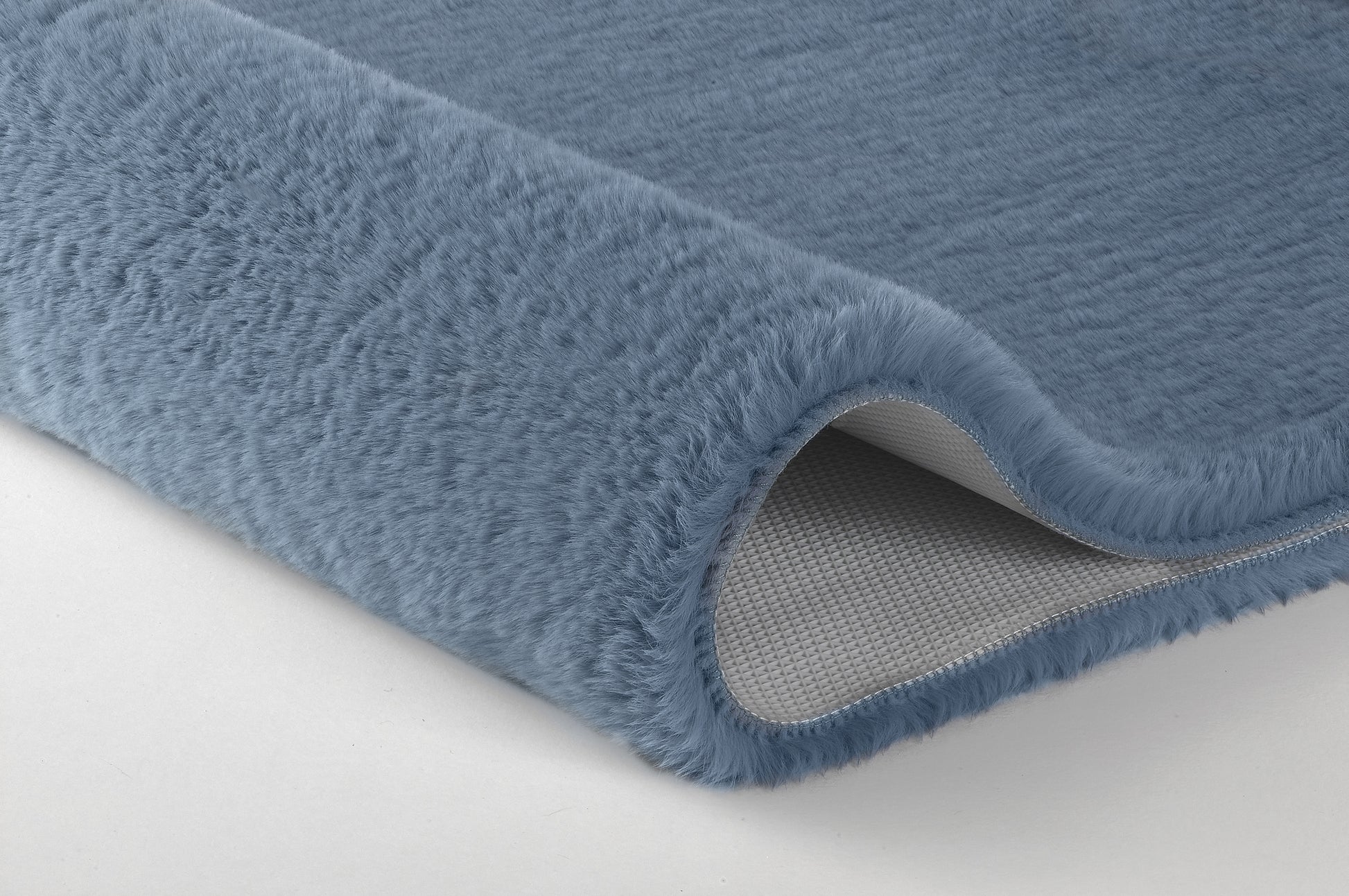 Detailansicht einer blauen, flauschigen Badematte mit abgerollter Kante