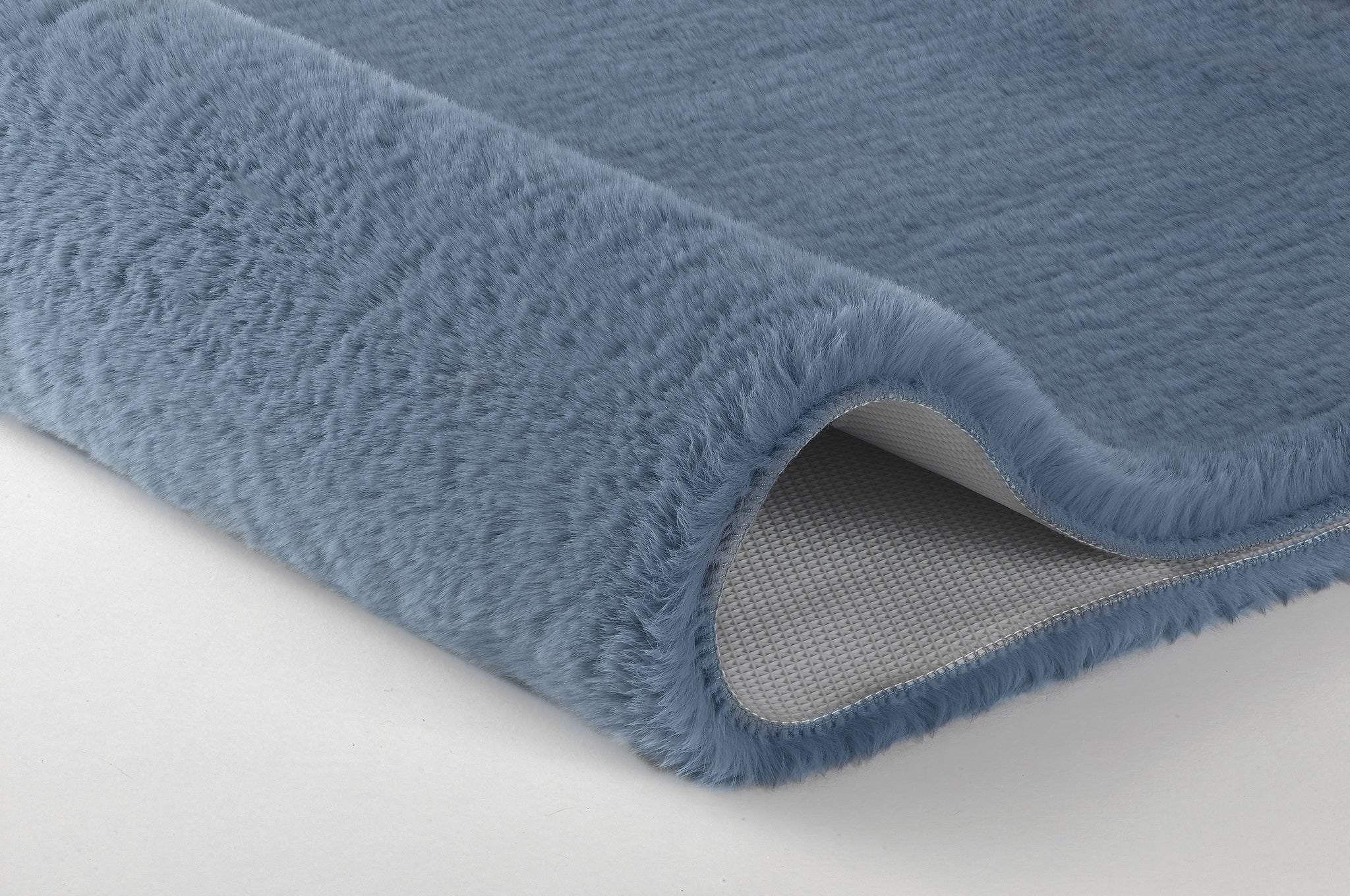 Detailansicht einer blauen, flauschigen Badematte mit abgerollter Kante
