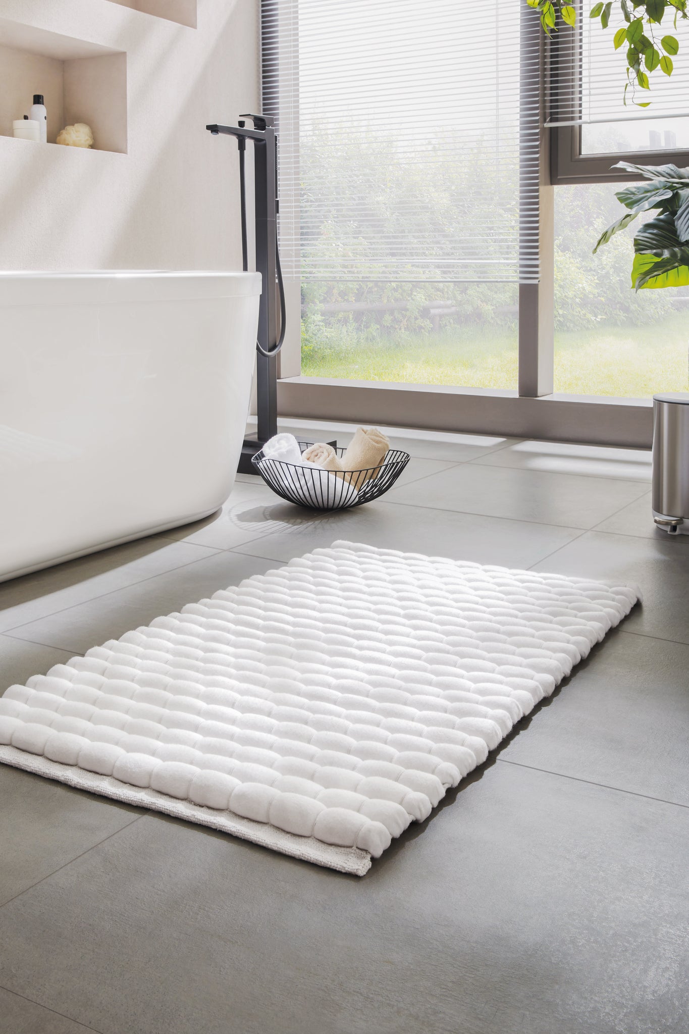 Weiße rechteckige Badematte vor Badewanne auf grauem Fliesenboden