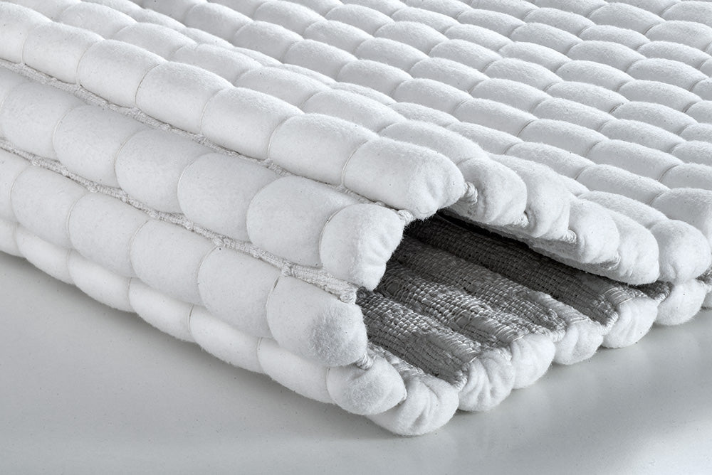 Gefaltete weiße Badematte mit gepolsterter Struktur, graue Unterseite