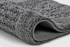 Graue, flauschige Badematte in Nahaufnahme, leicht dick eingerollt