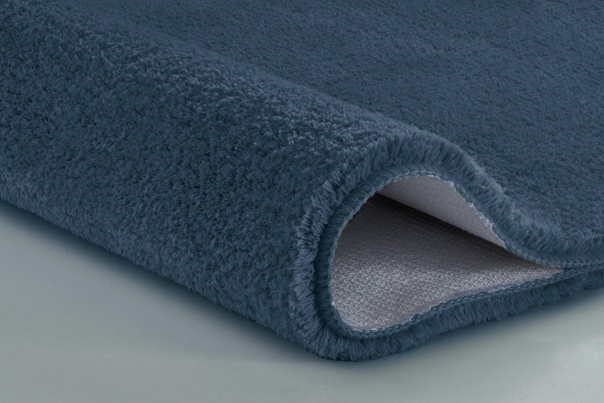Nahaufnahme einer dunkelblauen, flauschigen Badematte, aufgerollte Kante