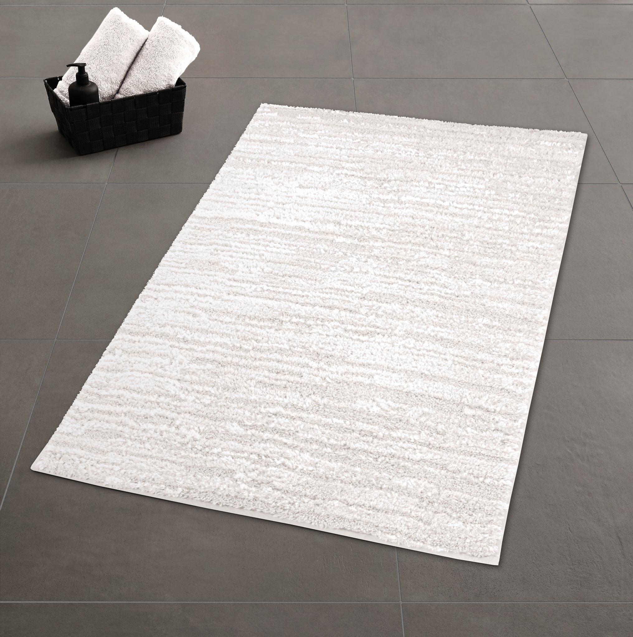 Heller, rechteckiger Badteppich auf grauen Fliesen, Korb mit Handtüchern