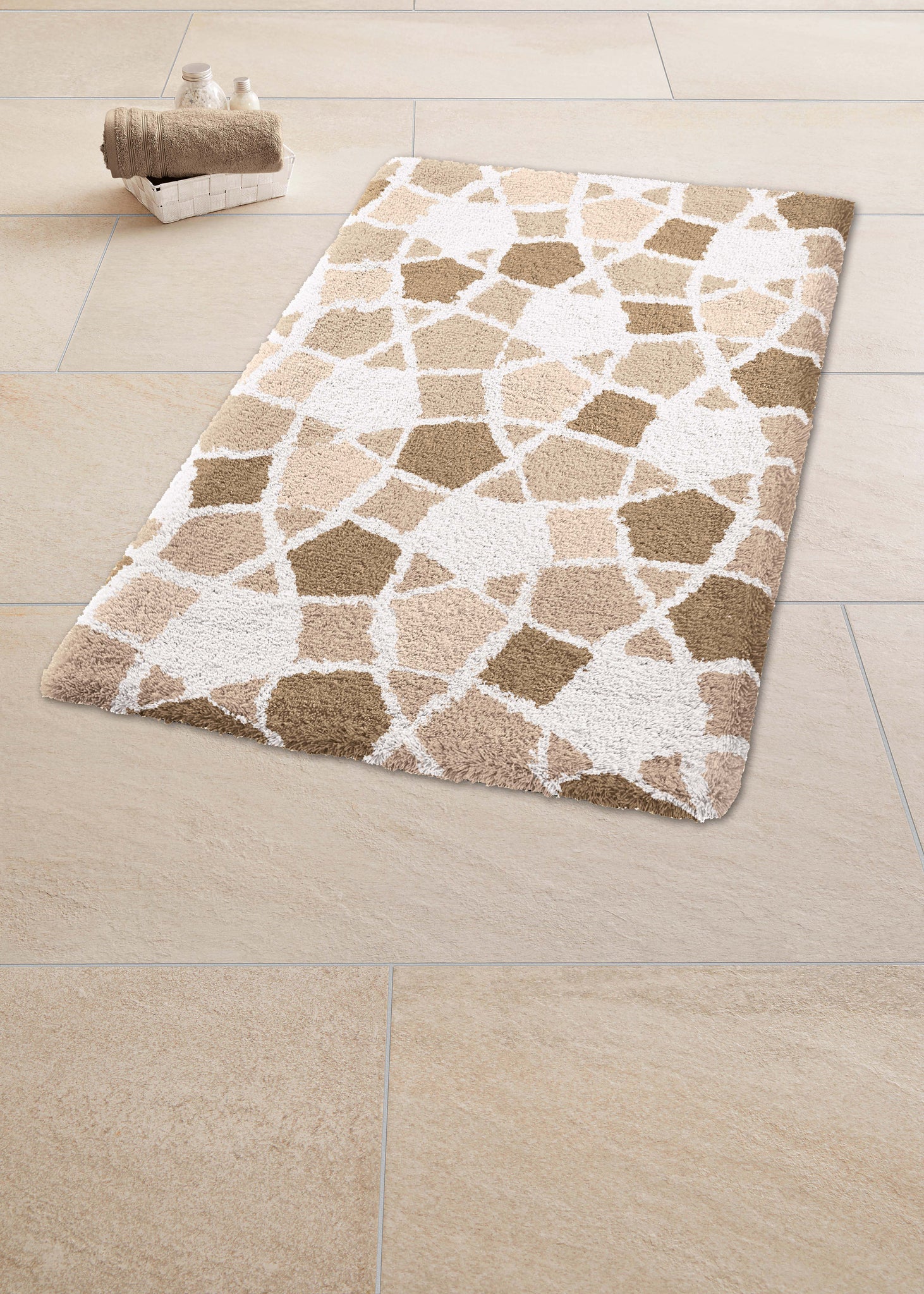 Badteppich SINTRA Macadamia 60 x 90 cm liegt auf hellen Fliesen neben einem Korb mit Handtüchern.
