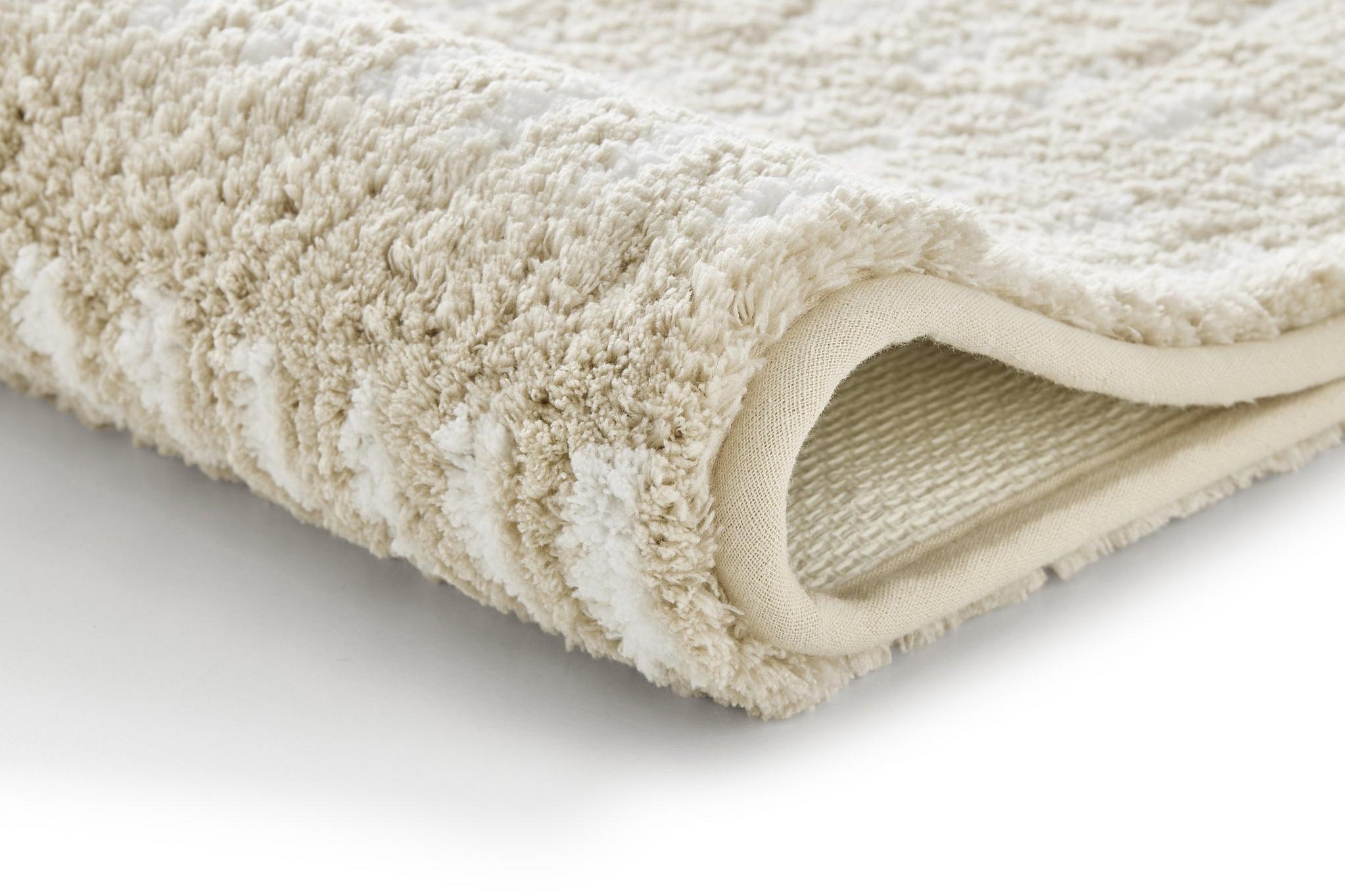 Beige Badematte mit Struktur, Nahaufnahme einer gefalteten Frottee-Ecke