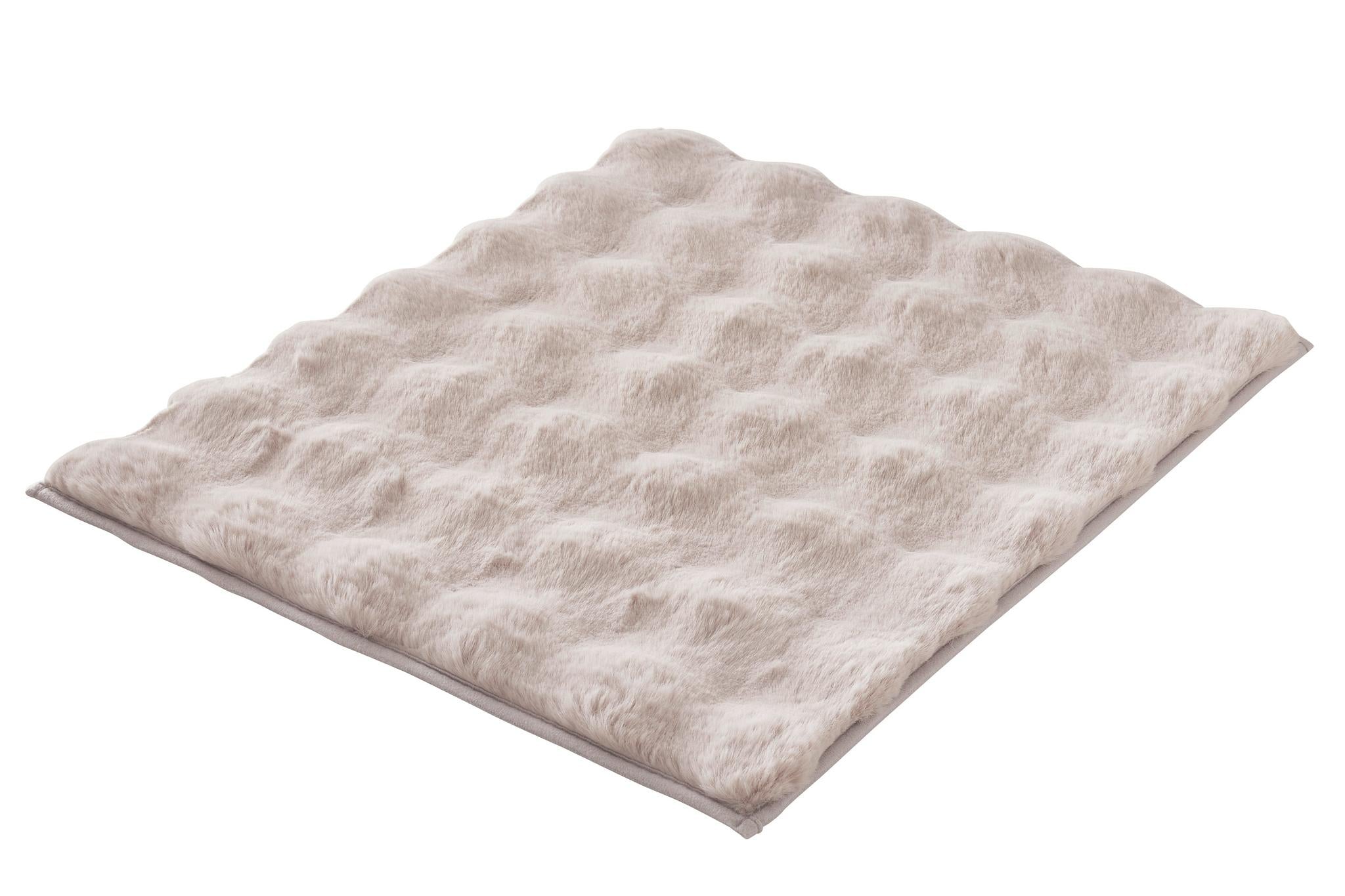 Beige, flauschige Badematte mit Wellenstruktur auf weißem Hintergrund