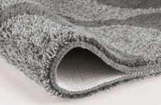 Nahaufnahme einer grauen, weichen Badematte mit umgeschlagener Ecke