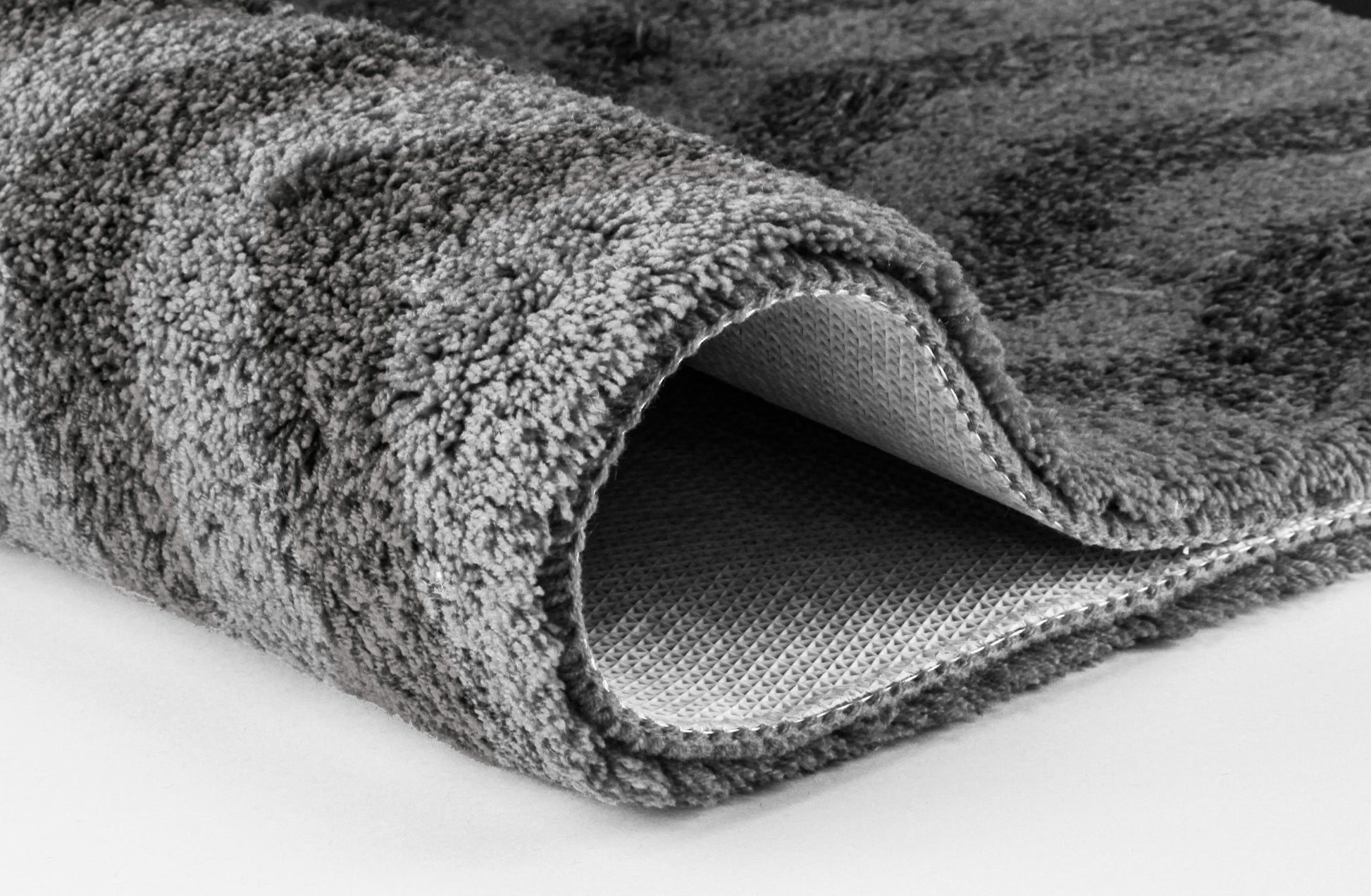 Graue, weiche Badematte in Nahaufnahme, eingerollte Kante sichtbar