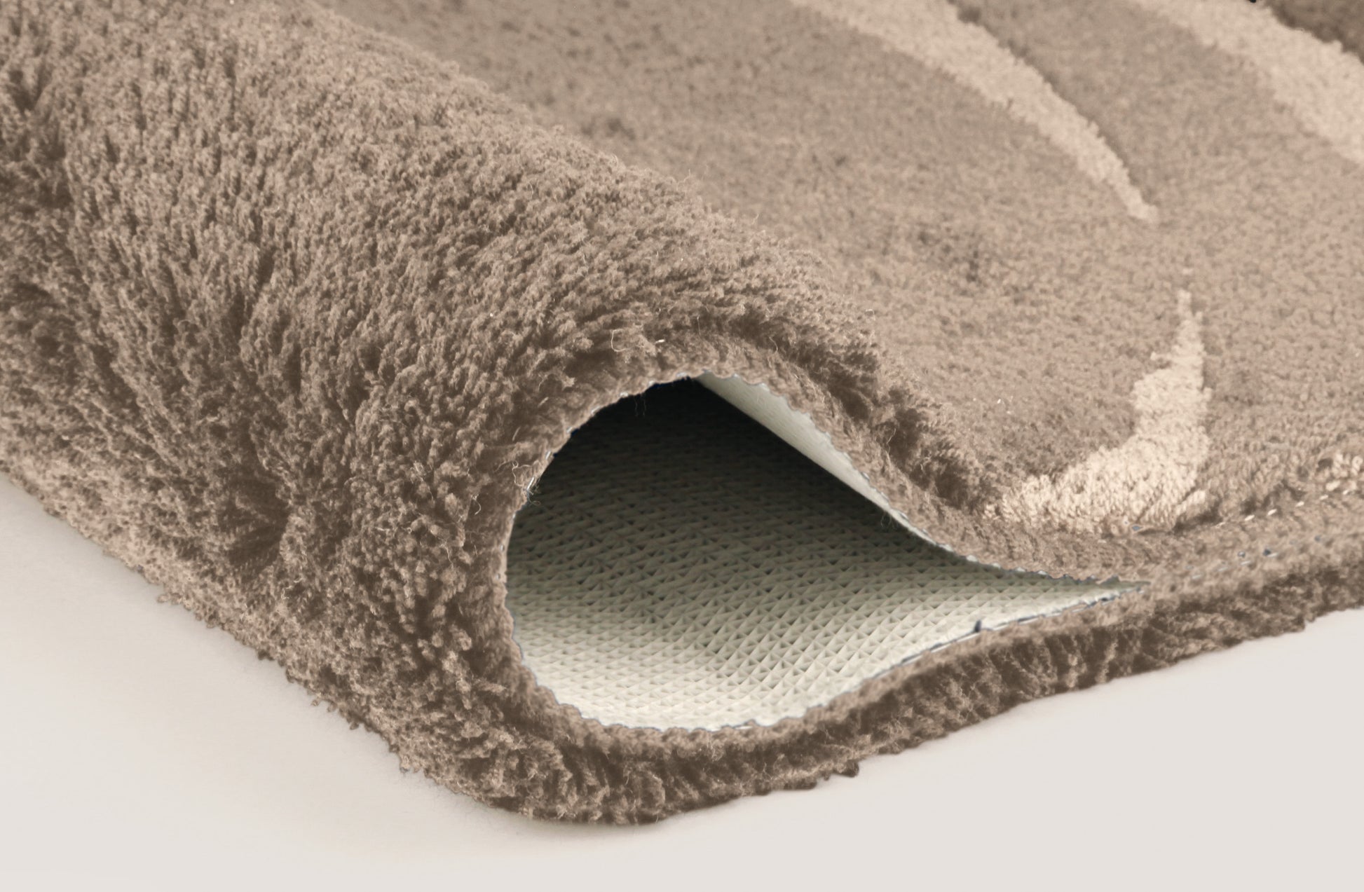 Nahaufnahme einer aufgerollten, beigefarbenen Badematte mit Rückseite