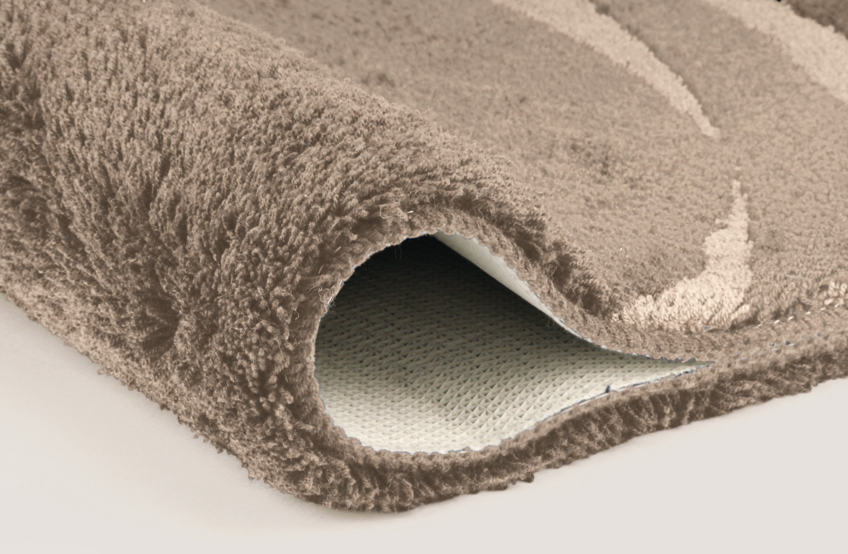 Nahaufnahme einer aufgerollten, beigefarbenen Badematte mit Rückseite