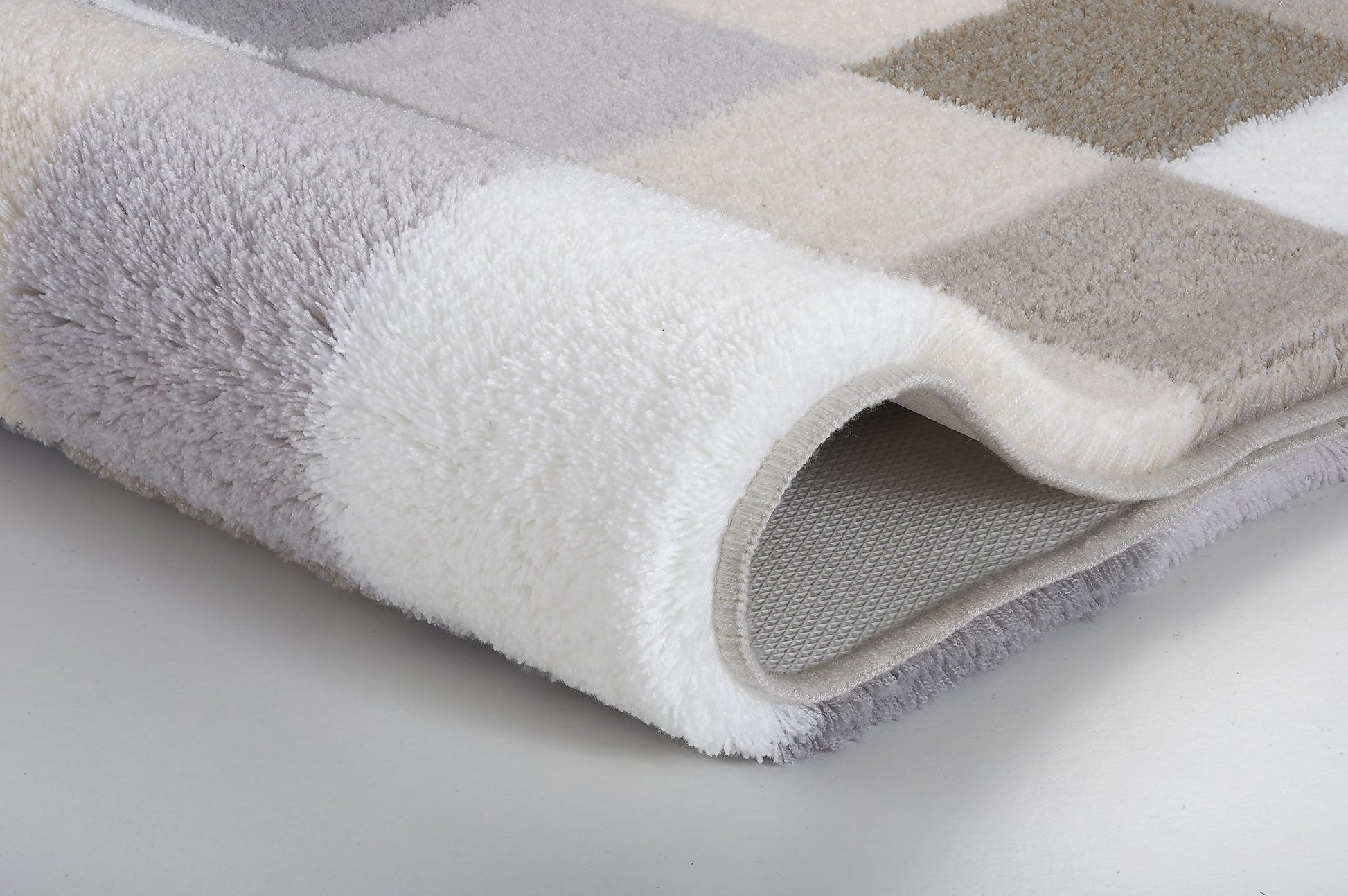 Badteppich CARO kaschmirfarben mit Karomuster in Grau, Beige und Weiß liegt gefaltet auf hellem Boden.