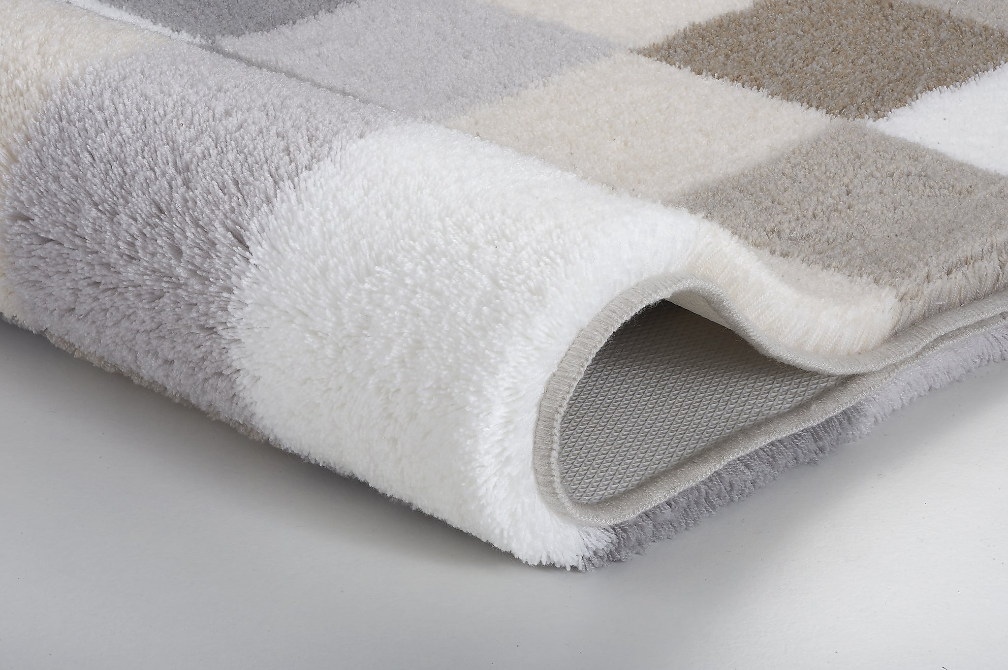 Badteppich CARO kaschmirfarben mit Karomuster in Grau, Beige und Weiß liegt gefaltet auf hellem Boden.