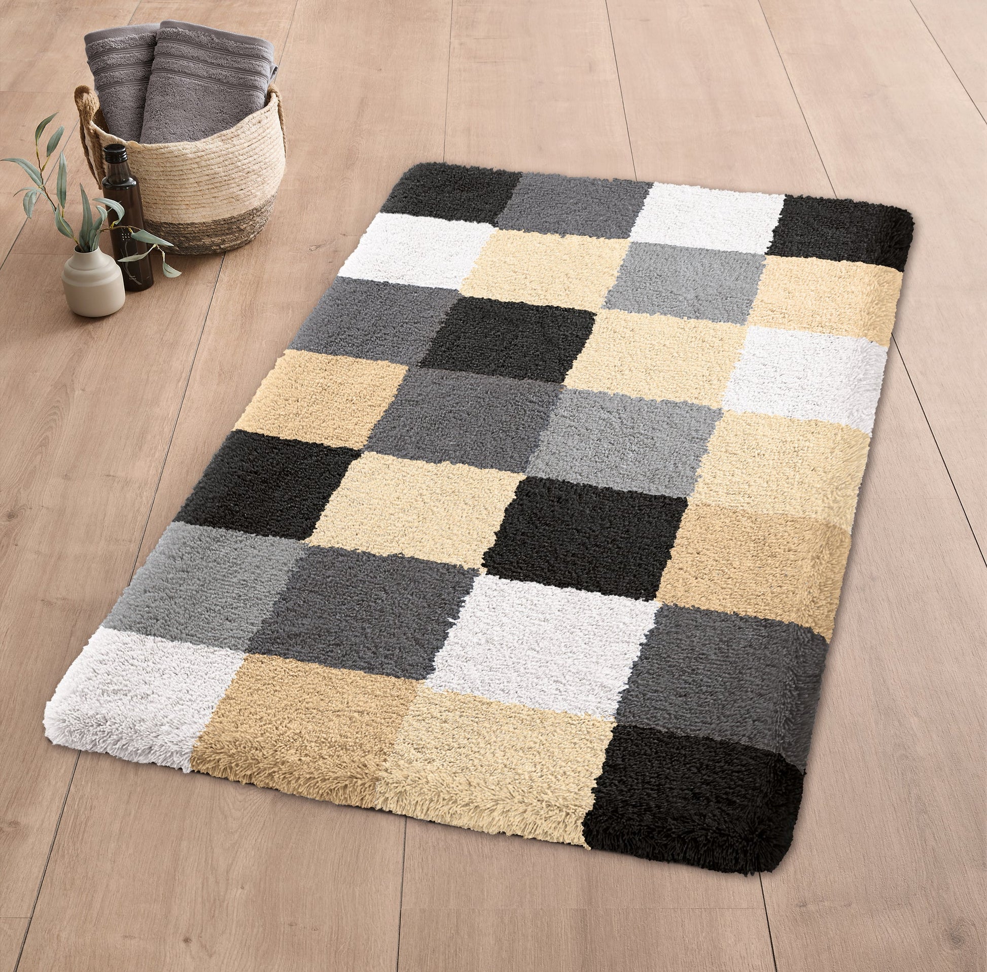 Badteppich CARO Schwarz 60 x 105 cm liegt auf Holzfußboden mit Korb und Handtüchern daneben.