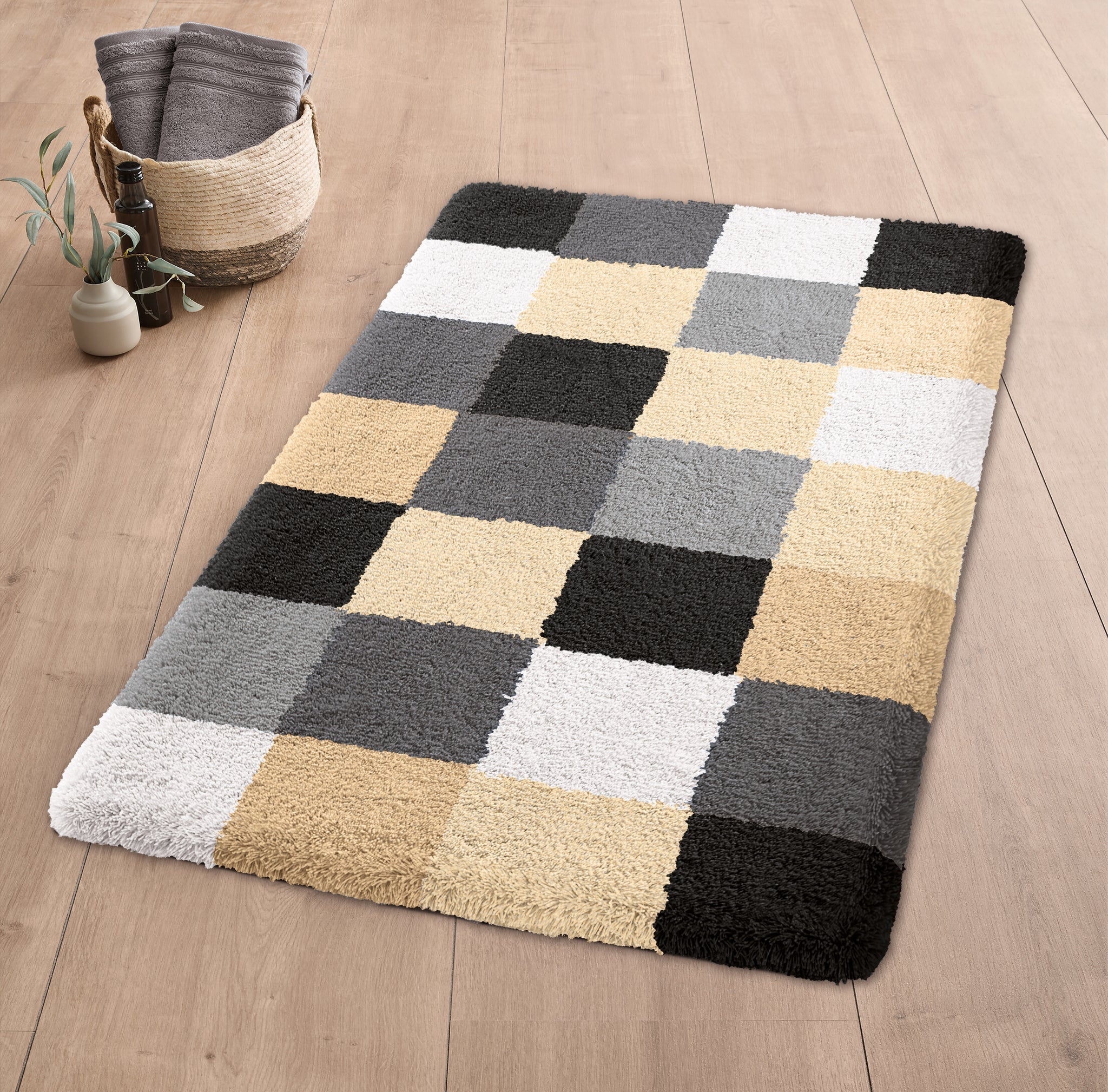 Badteppich CARO Schwarz 60 x 105 cm liegt auf Holzfußboden mit Korb und Handtüchern daneben.