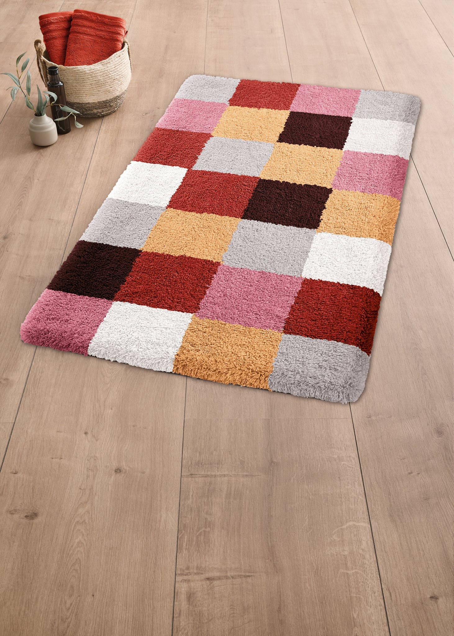 Badteppich CARO Terracotta 70x120 liegt im Bad auf Holzfußboden neben Korb und Pflanze.