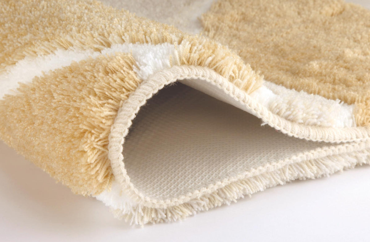 Zusammengerollter cremefarbener Badteppich mit weichem Flor in Nahaufnahme.