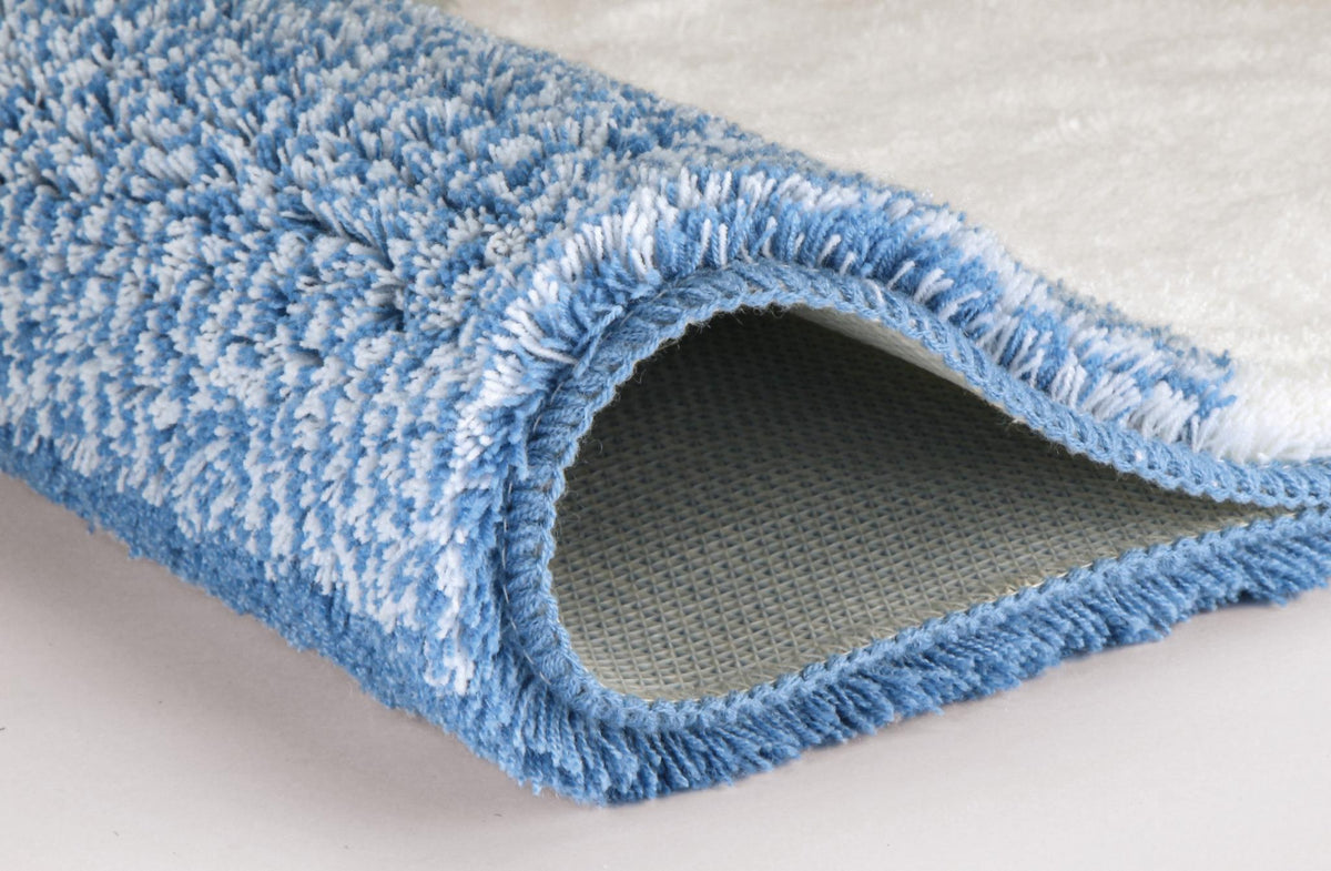 Zusammengerollter hellblauer Hochflor-Badteppich mit rutschfester Unterseite.